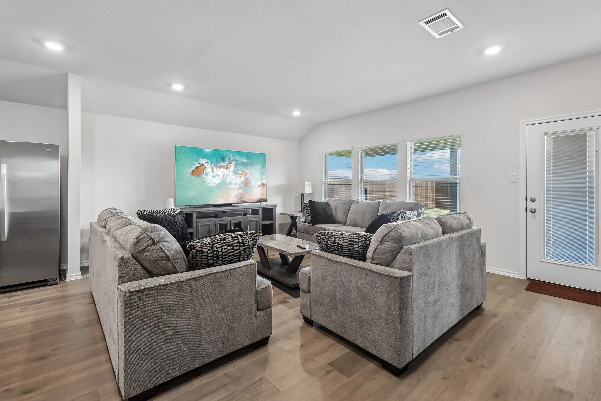 Spacious open-concept living area featuring wood-finish flooring, recessed lighting, and a wall of windows