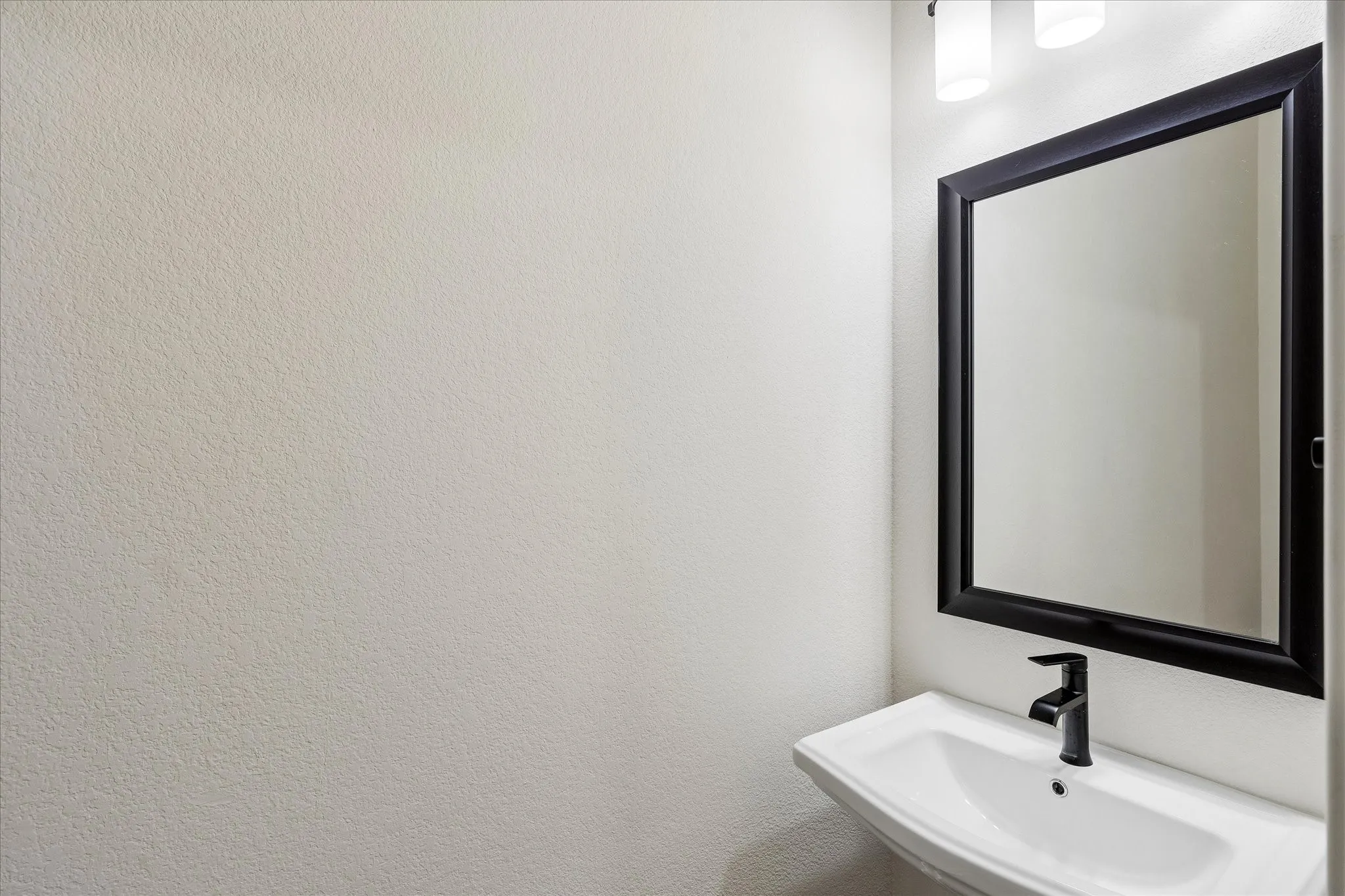 Modern wall-mounted sink with a matte black faucet, framed mirror, and contemporary vanity lighting