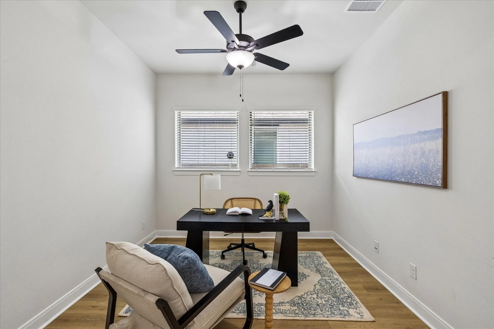 Bright room with wood-finish flooring, two windows with blinds, a ceiling fan with integrated lighting, and white baseboards
