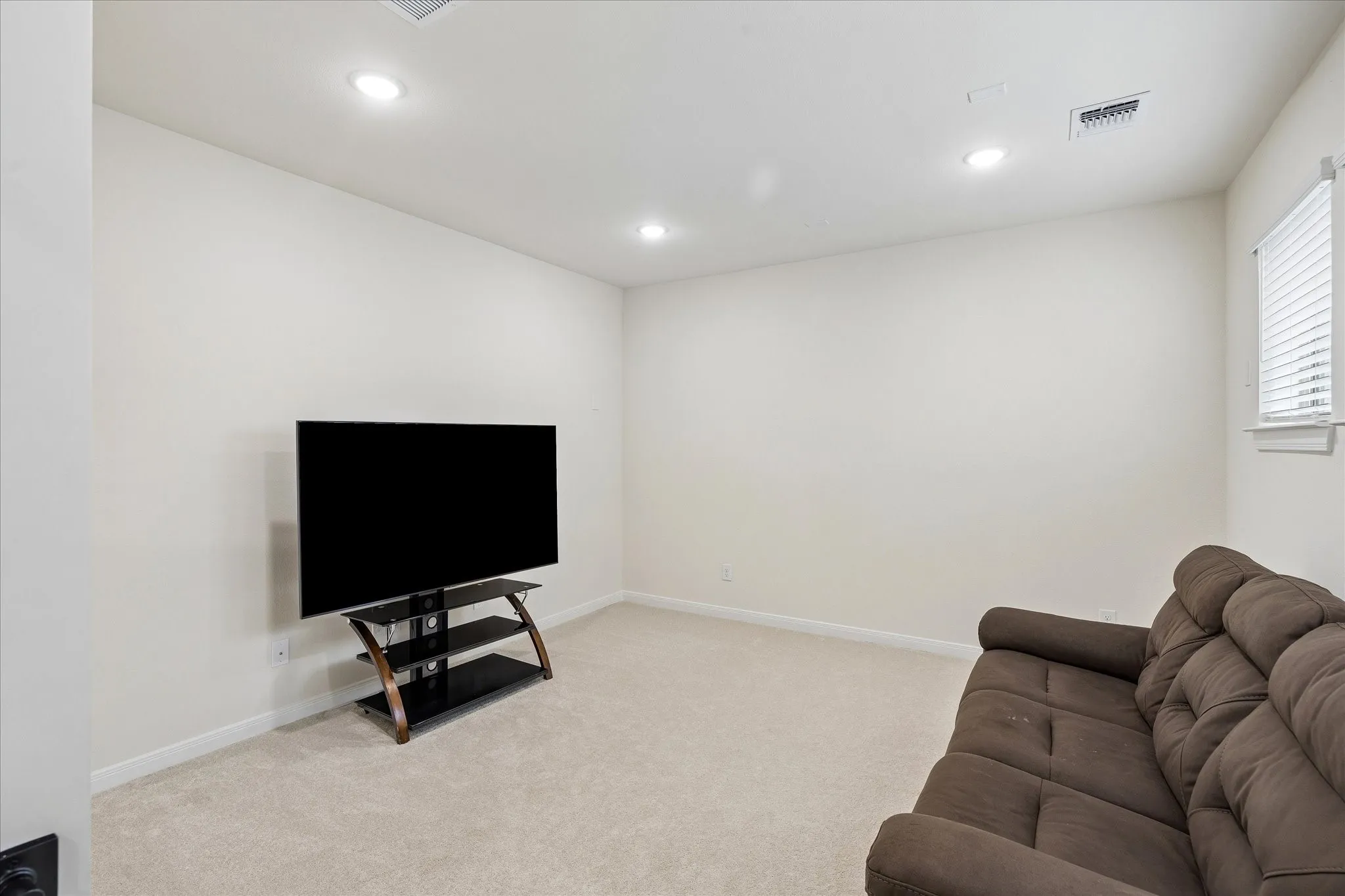 Recessed lighting illuminates the neutral wall tones and light-colored carpeting in this versatile space