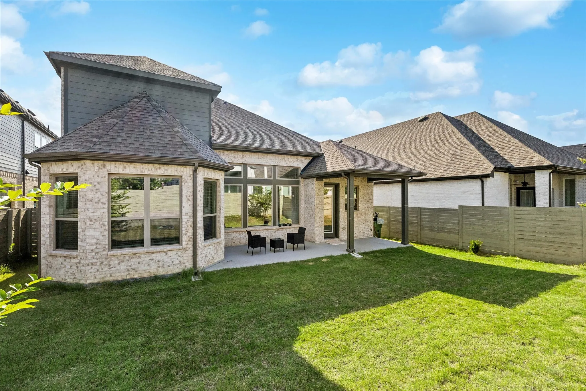 Expansive green lawn with a covered patio, brick and siding exterior, multiple windows, and a privacy fence