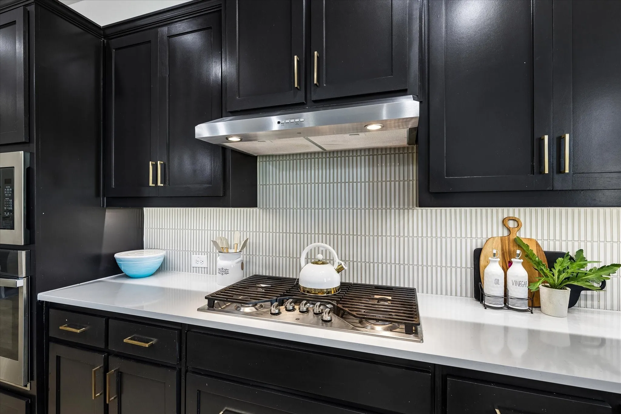 Kitchen featuring black cabinetry with gold-finish hardware, light-toned countertops, and a full-height tile backsplash