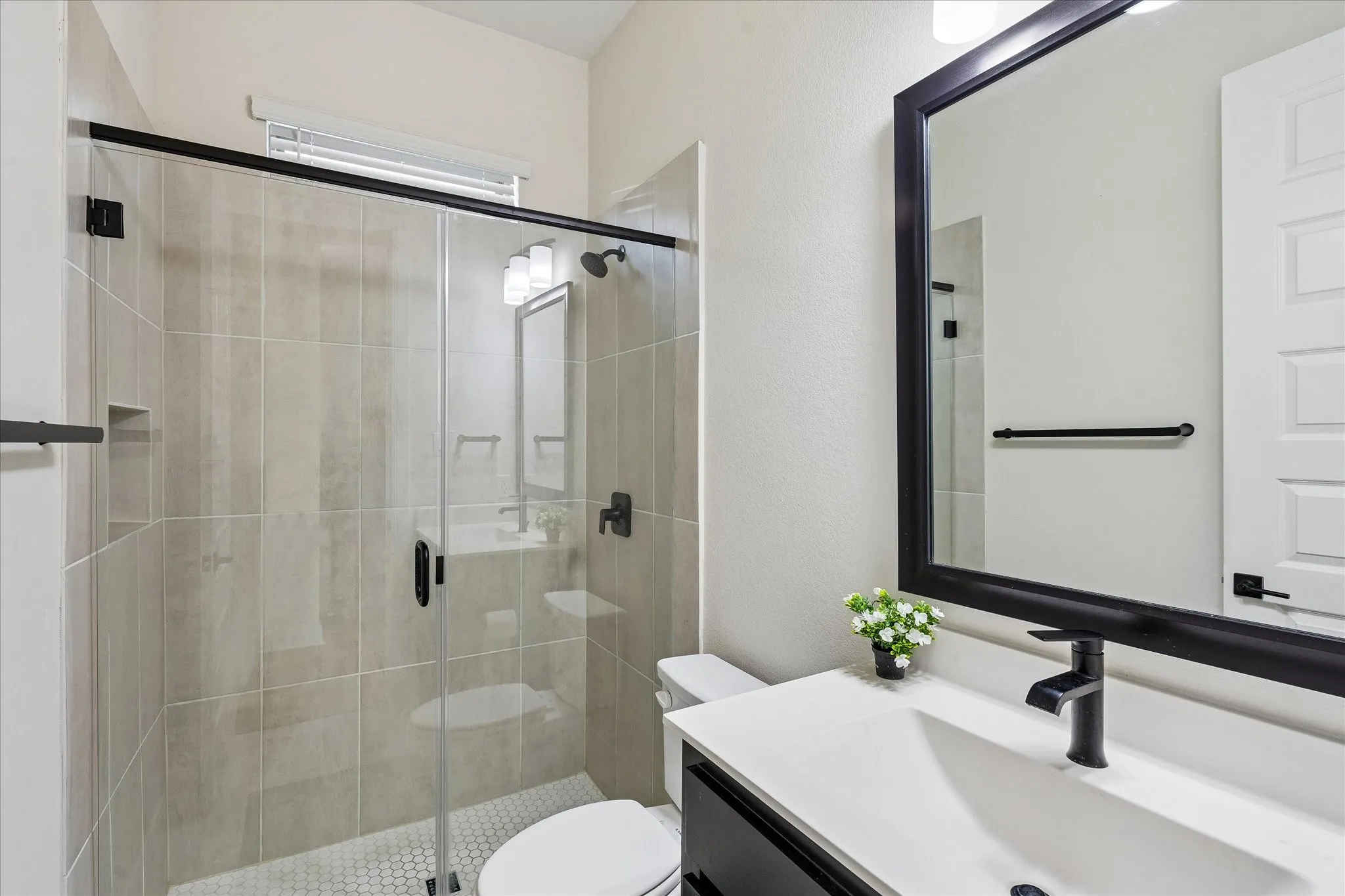 Bathroom with a frameless glass shower enclosure featuring large-format wall tiles and a hexagonal floor tile
