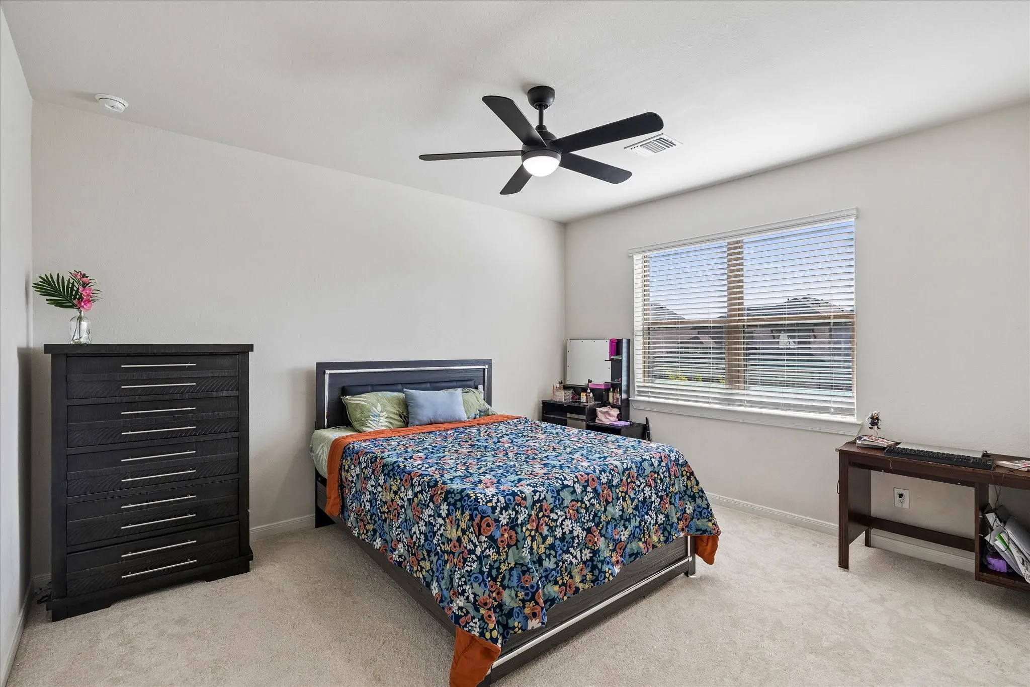 Carpeted bedroom featuring a large window with blinds, a ceiling fan with integrated lighting, and neutral wall tones
