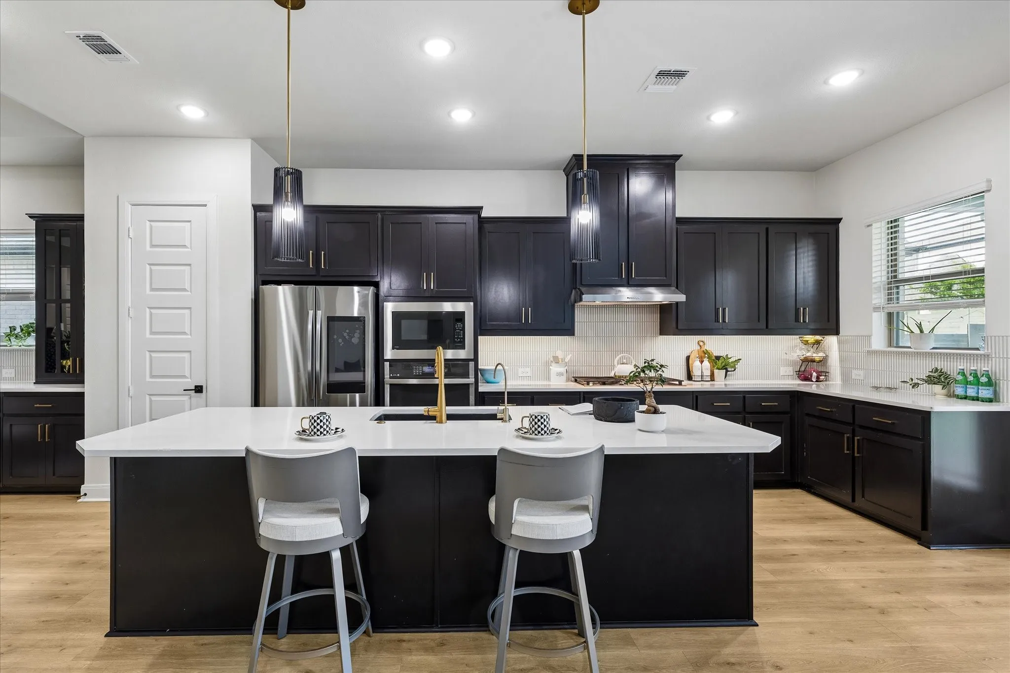 Modern kitchen featuring a large central island with seating, dark cabinetry, stainless steel appliances, light countertops, and wood-finish flooring