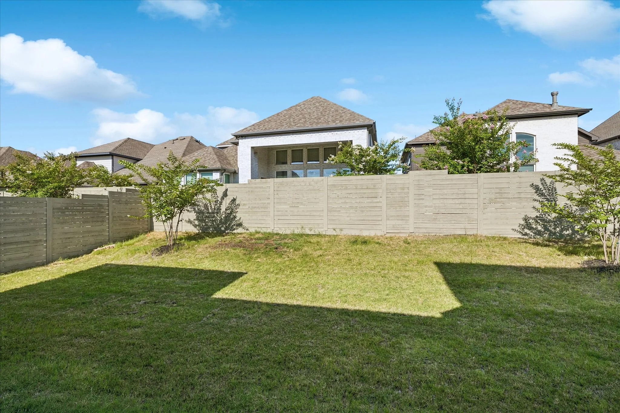 Expansive backyard featuring a lush lawn, mature trees, and a horizontal slatted privacy fence