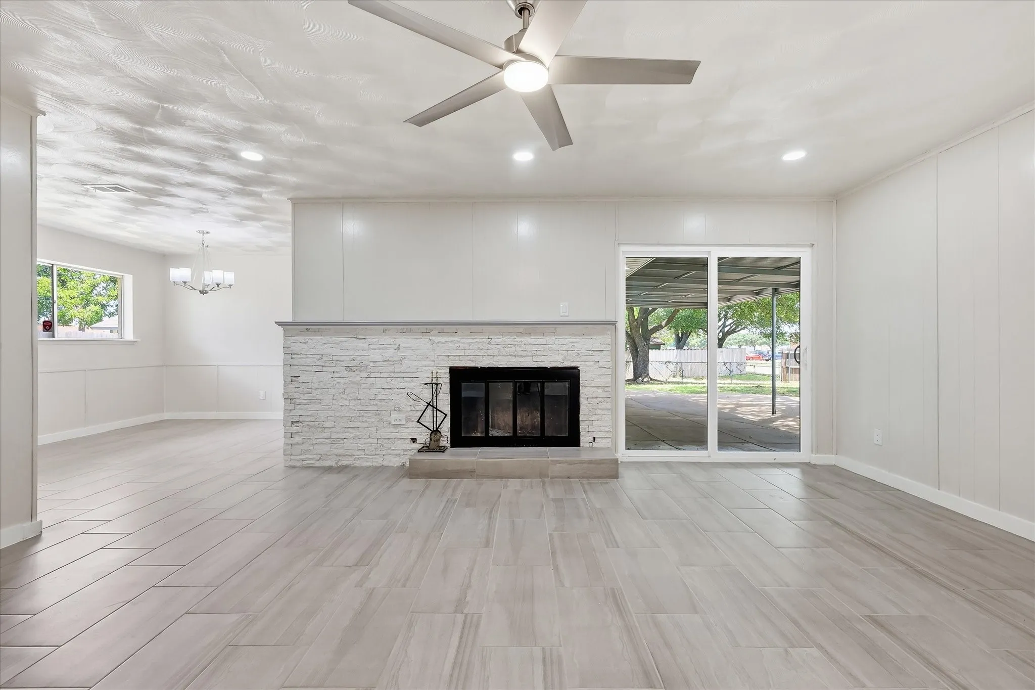 Spacious living area featuring wood-look tile flooring, a white brick fireplace with a stone mantel, recessed lighting, and a ceiling fan
