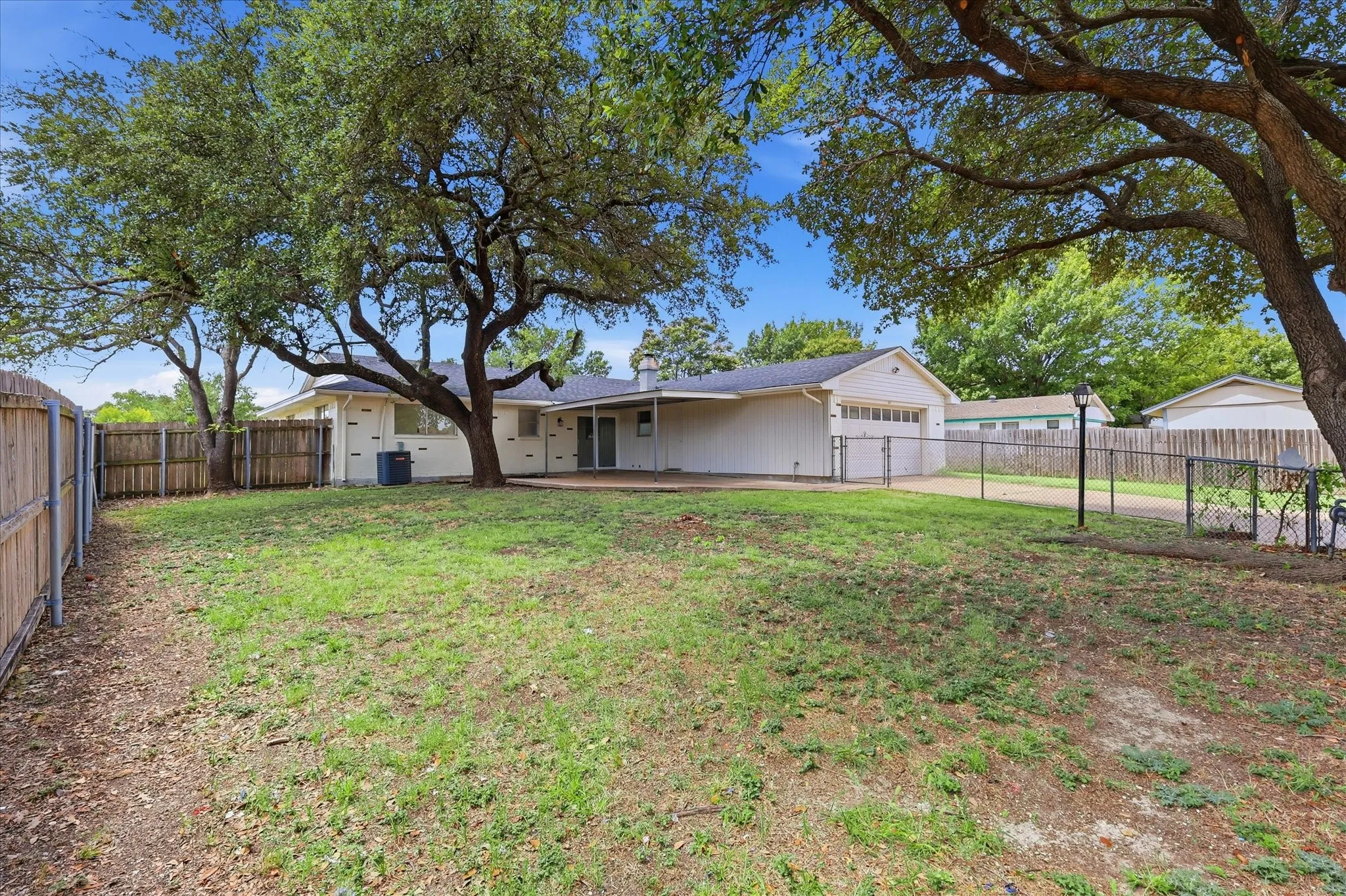 Expansive backyard featuring mature trees, a wooden privacy fence, chain-link fencing, and a concrete patio
