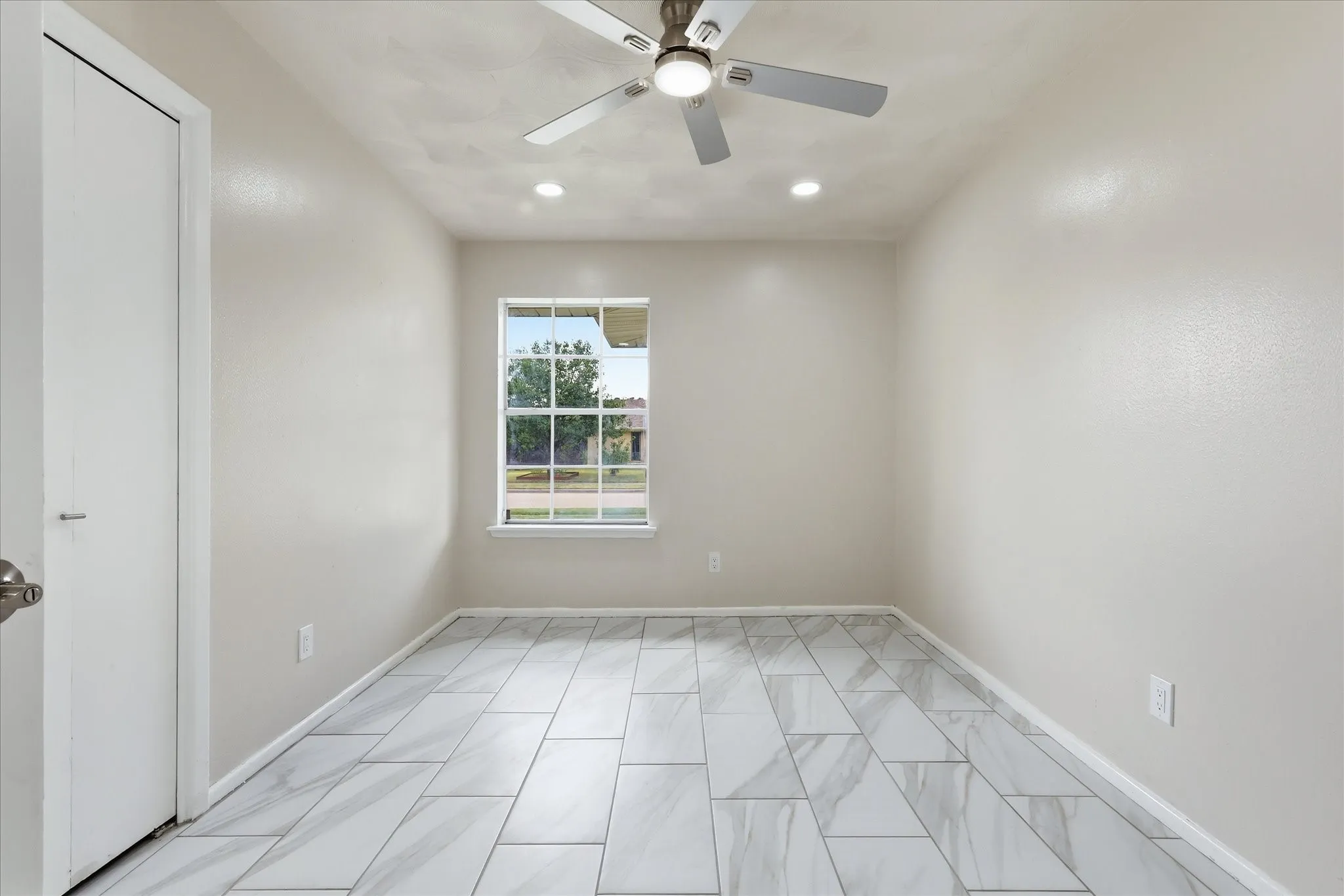 Room featuring large format tile flooring, a window with exterior views, a ceiling fan with integrated lighting, and recessed ceiling lights