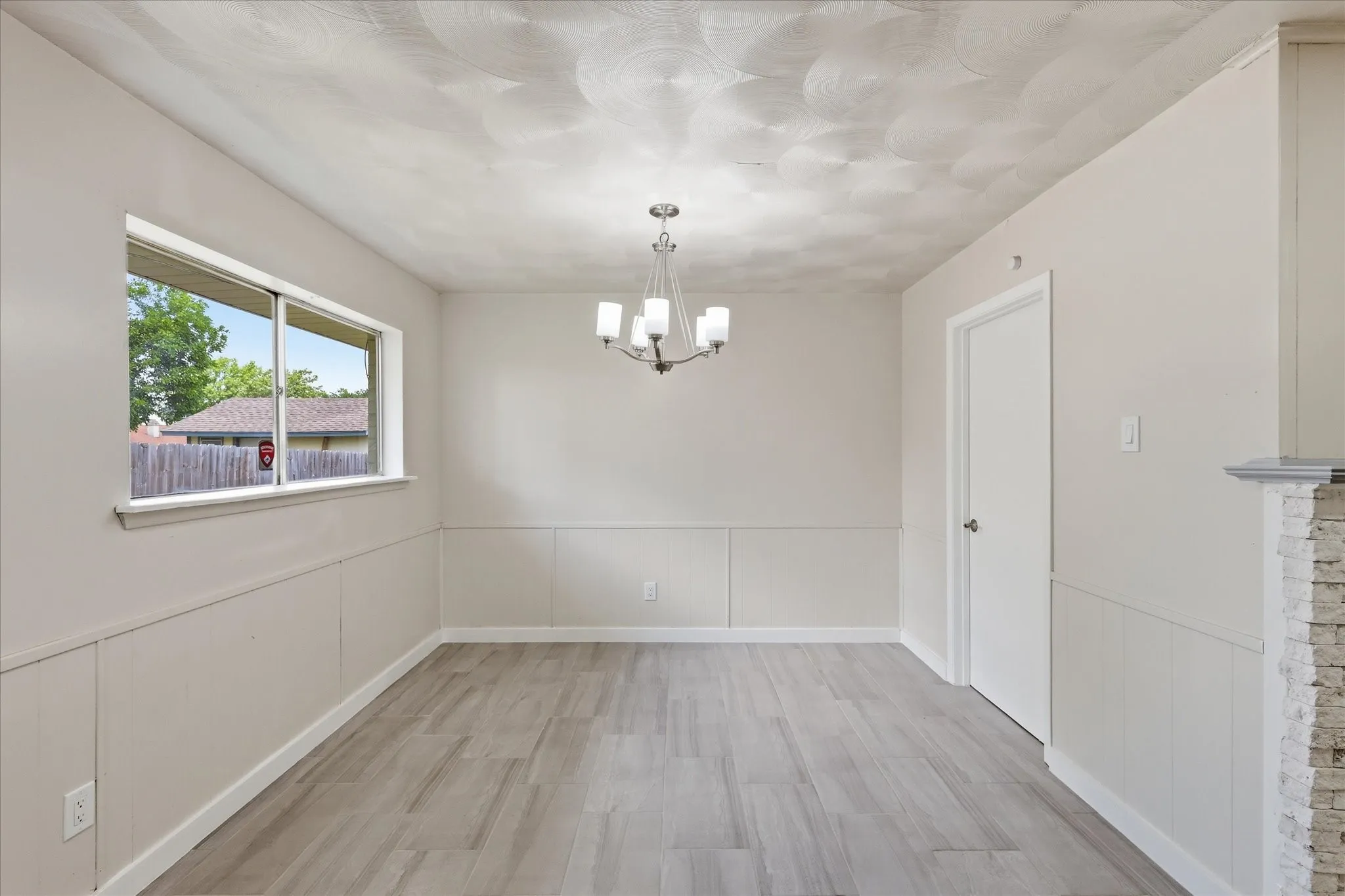 Spacious room featuring wood-finish flooring, wainscoting, and a multi-light chandelier