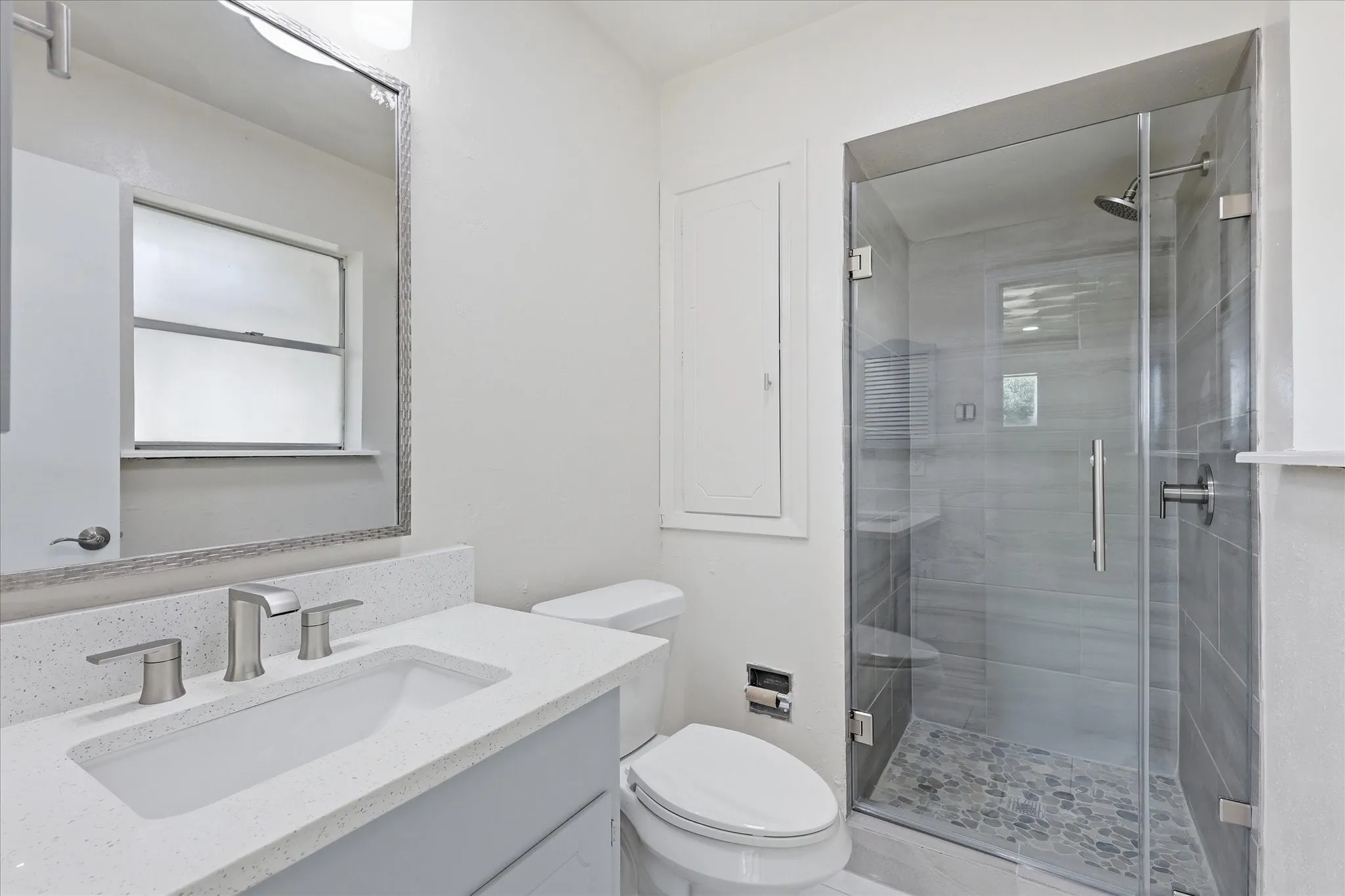Bathroom featuring a walk-in shower with glass enclosure, pebble stone shower floor, and gray subway tile surround