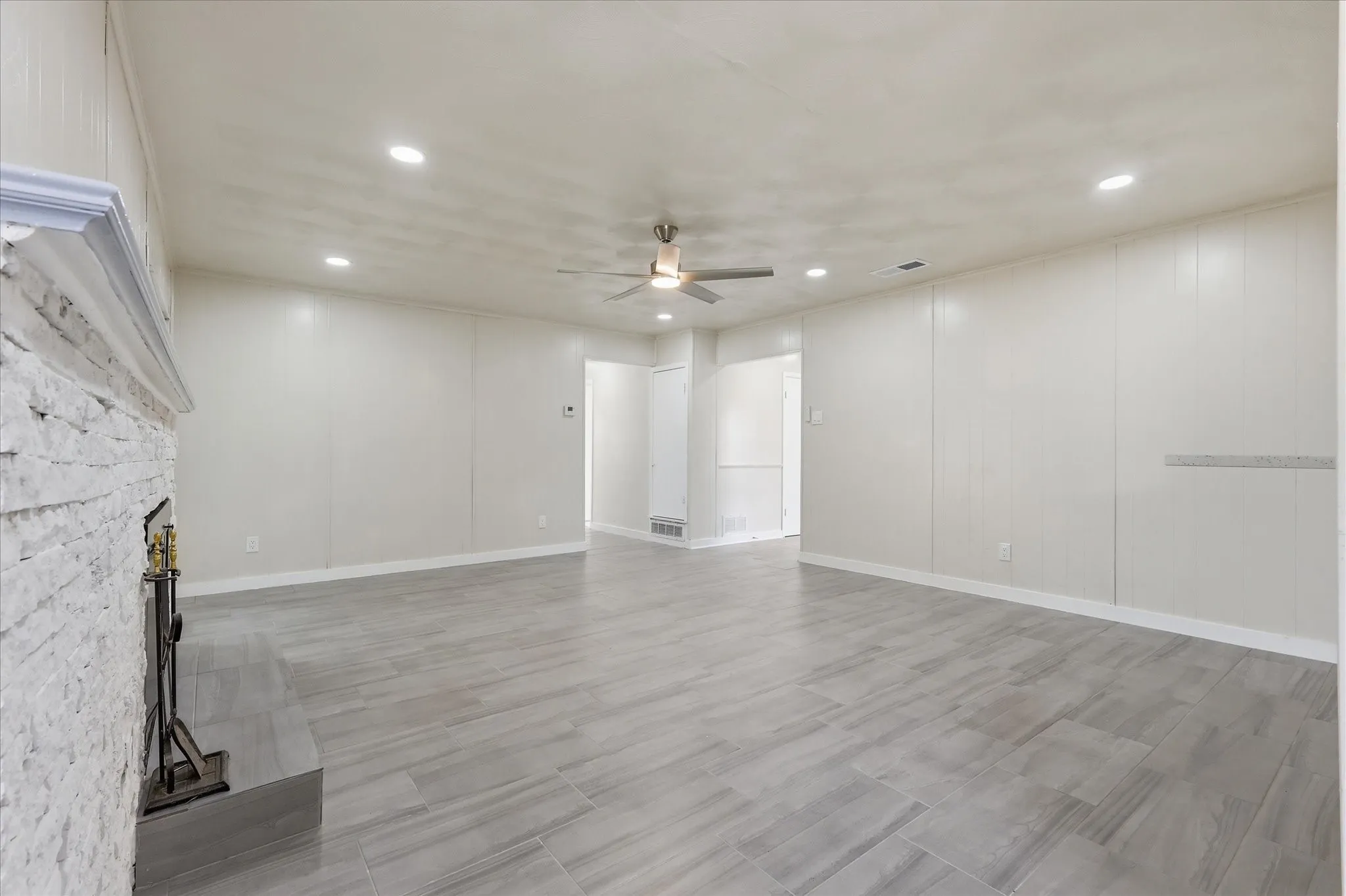 Spacious living area featuring a stacked stone fireplace with mantle, wood-finish tile flooring, recessed lighting, and a ceiling fan
