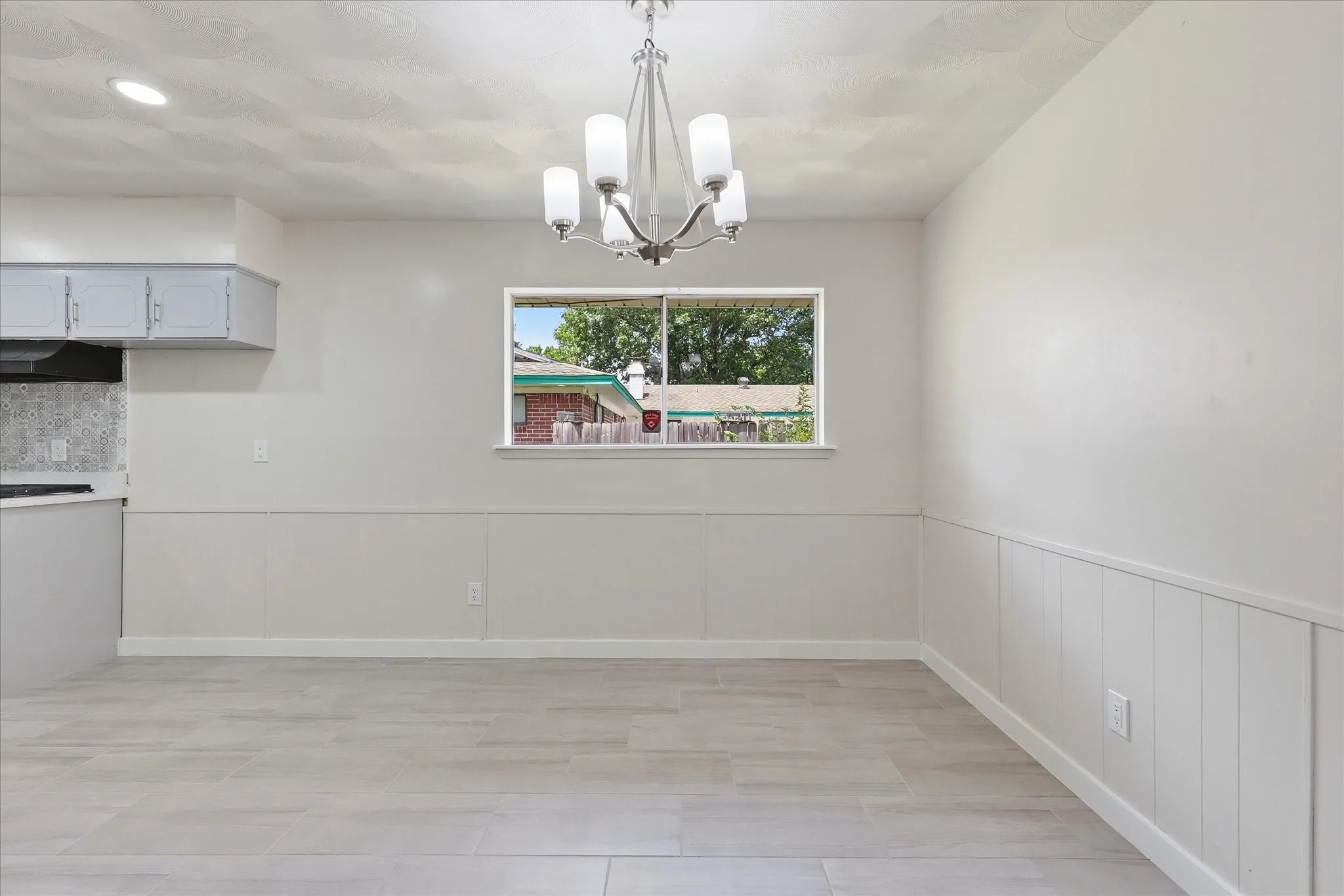 Dining area featuring a contemporary chandelier, light-toned wood-look tile flooring, and a window providing natural light
