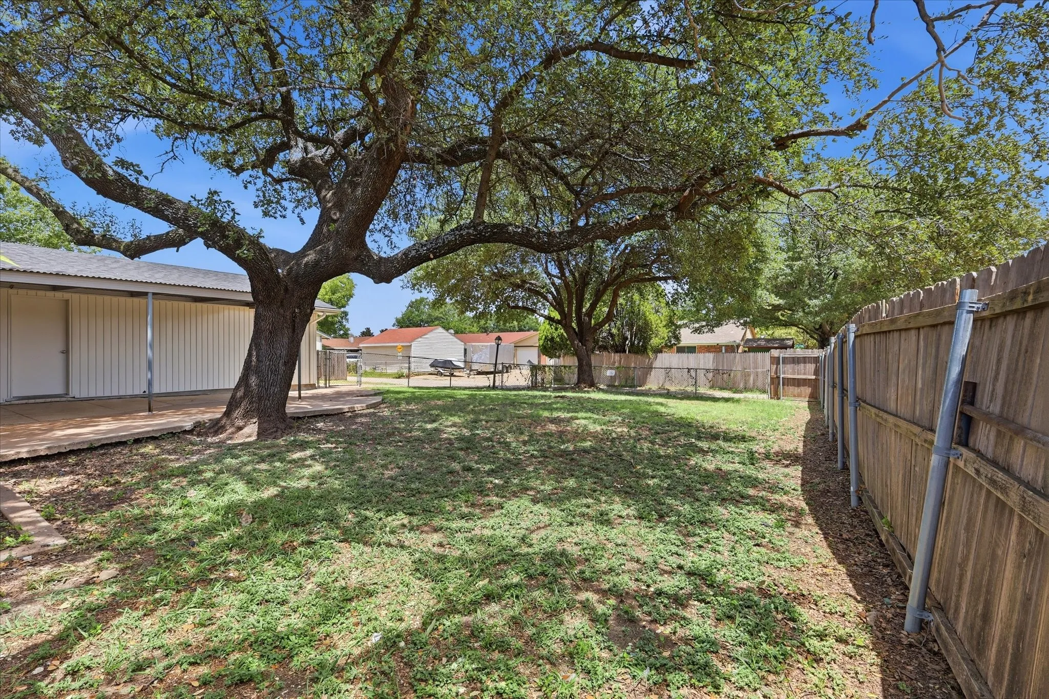 Spacious backyard featuring a prominent mature tree, natural grass, and a wood privacy fence