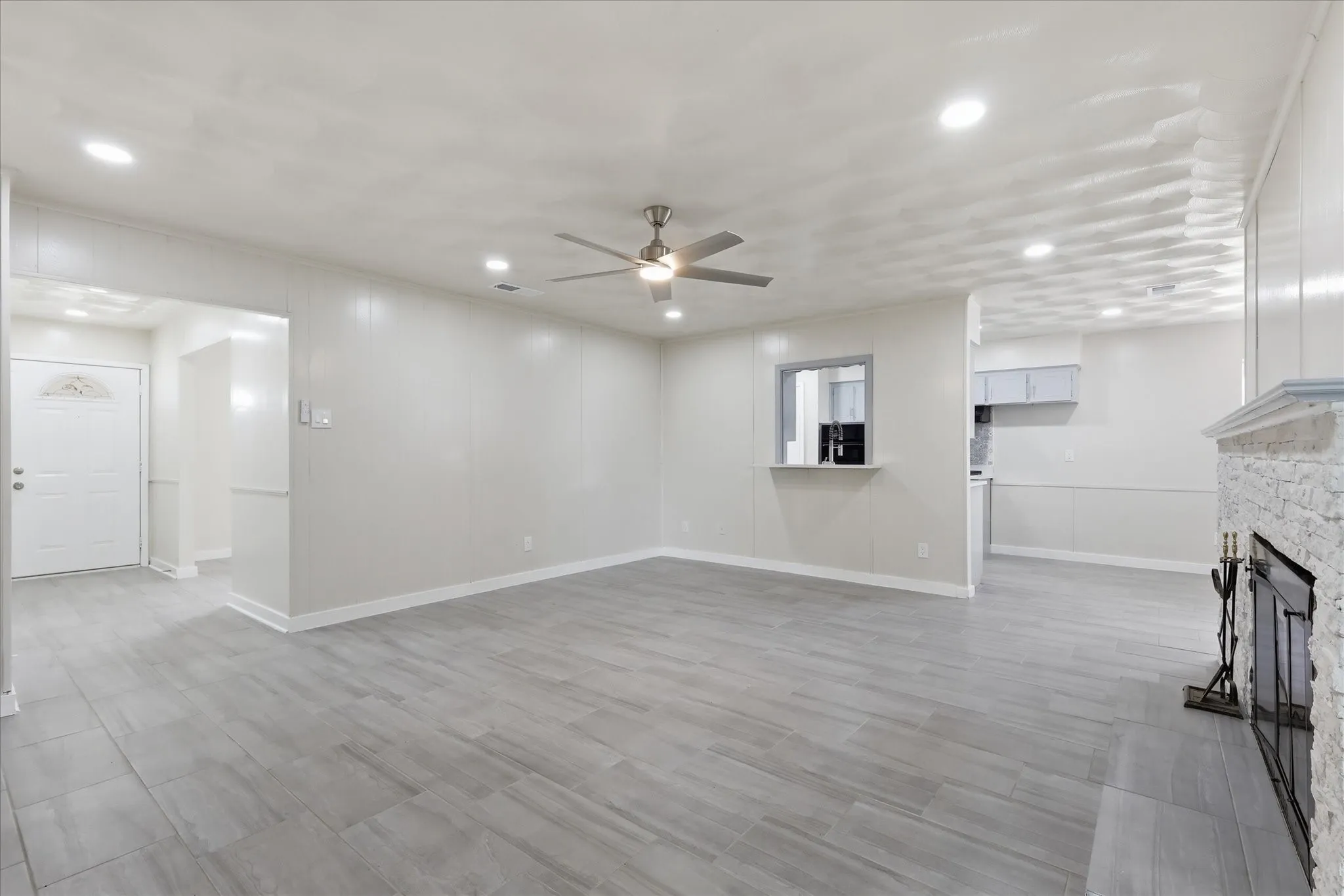 Spacious living area featuring light gray wood-finish flooring, recessed lighting, and a contemporary ceiling fan