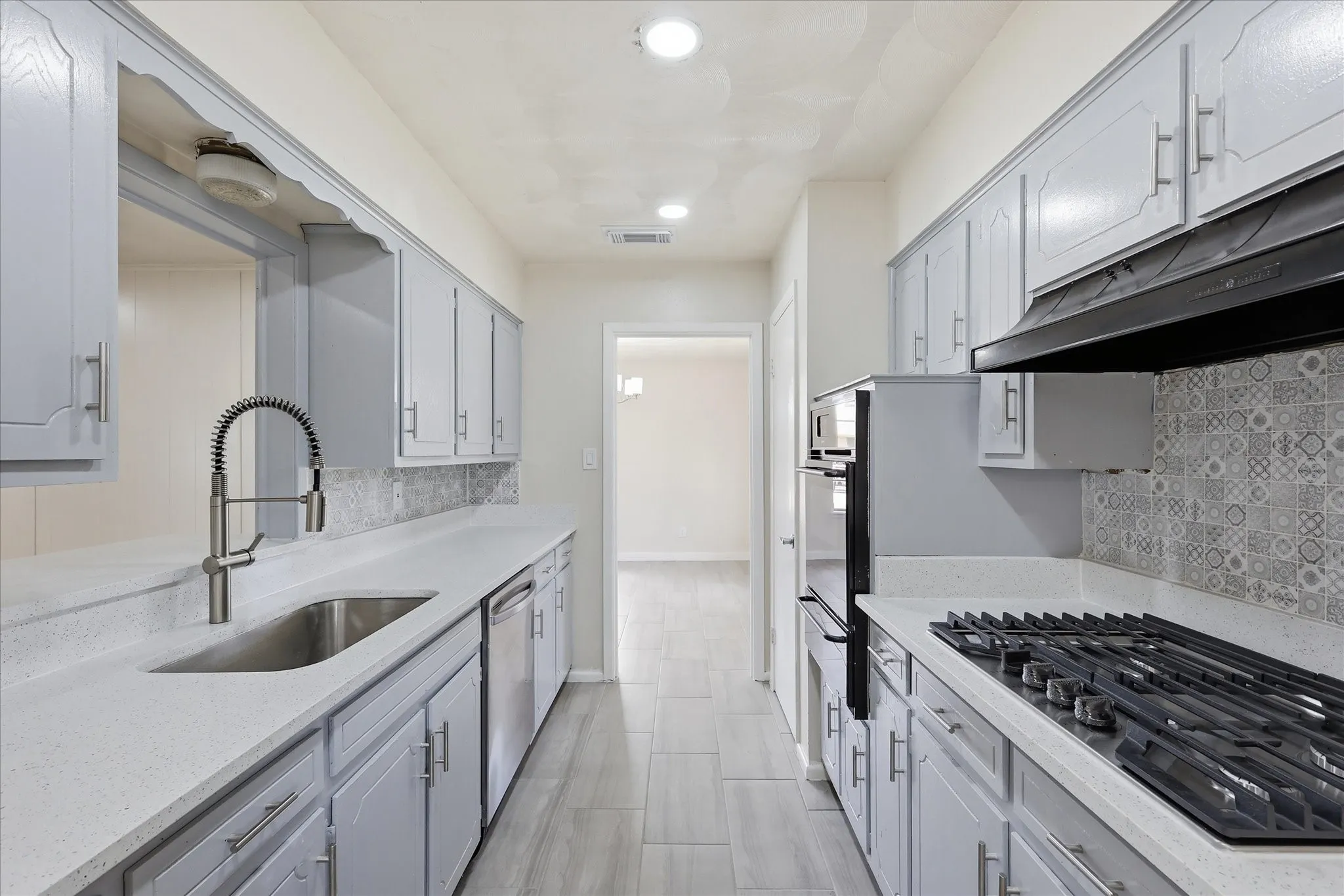 Galley kitchen featuring light gray cabinetry, light-toned countertops, and a decorative tile backsplash