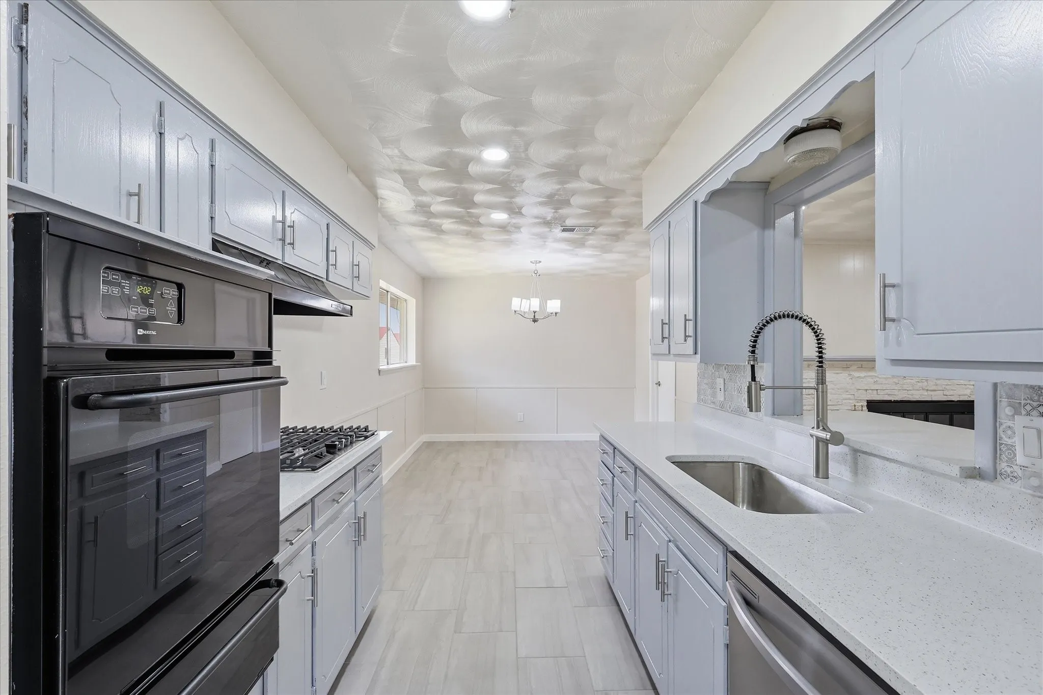 Galley kitchen featuring light-toned cabinetry, light-toned countertops, tile flooring, a built-in oven, and a gas cooktop