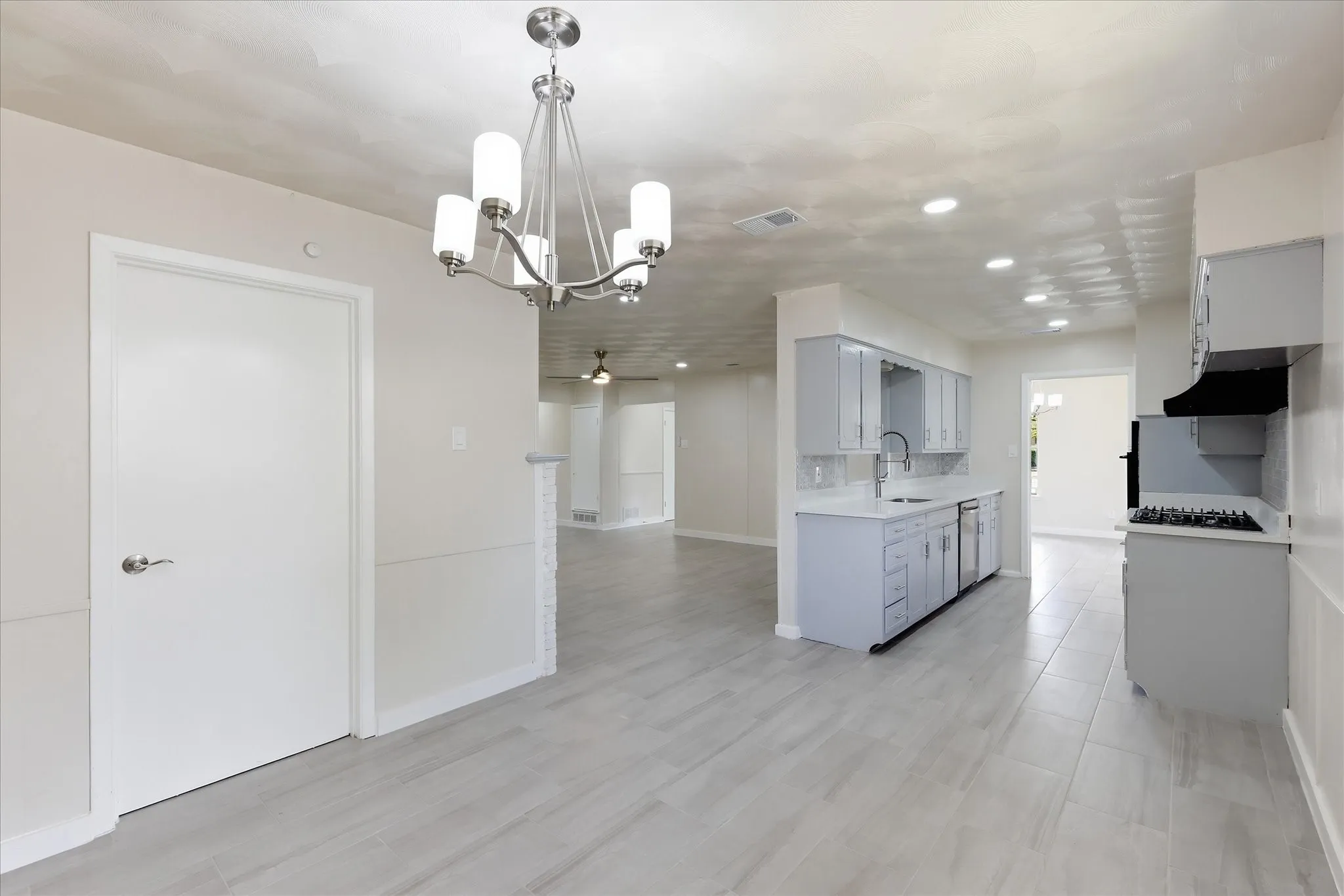 Open-concept living space featuring wood-finish flooring, a contemporary chandelier, recessed lighting, light-toned walls, and a modern kitchen with grey cabinetry and stainless steel appliances