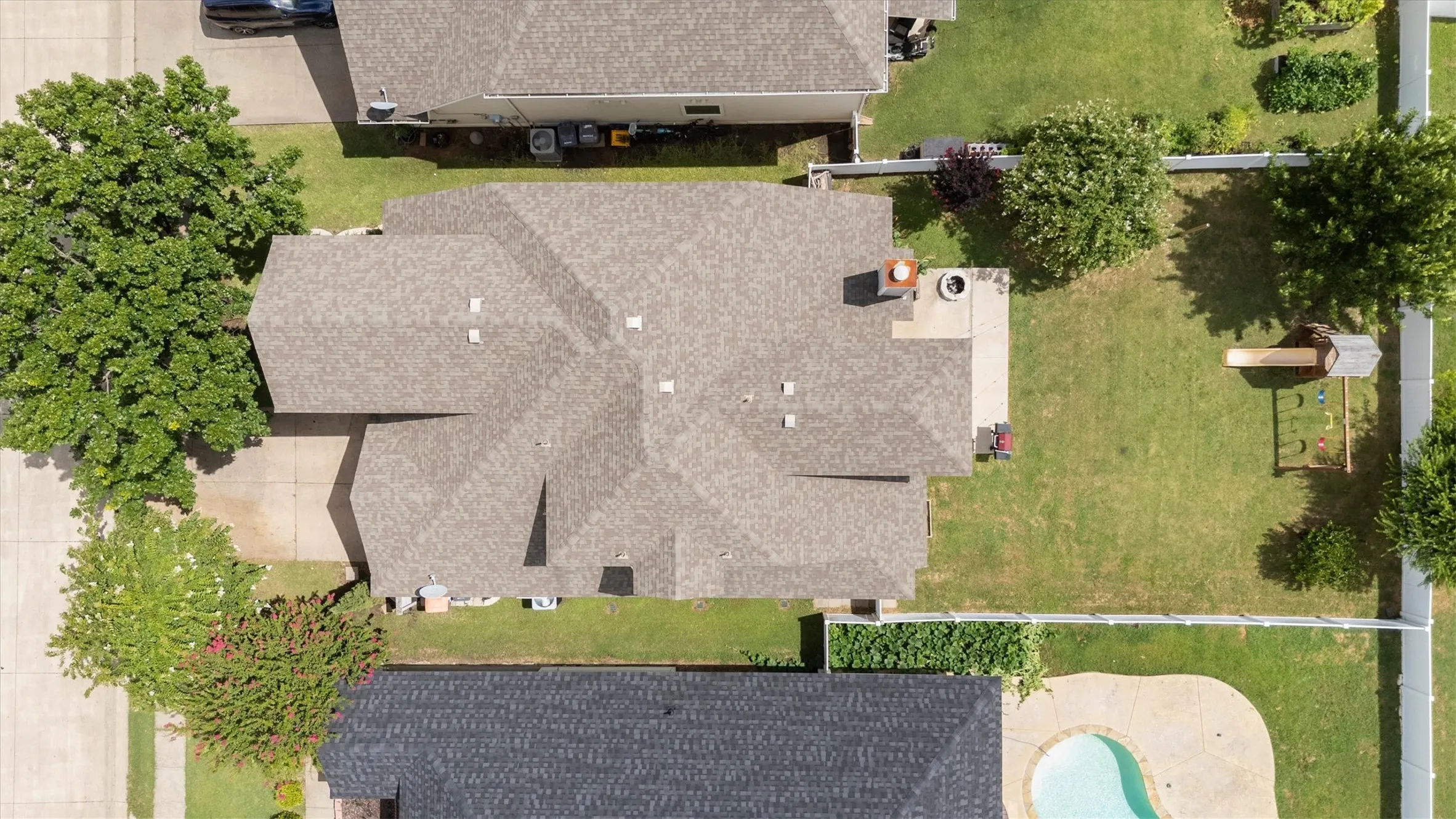 Expansive backyard featuring a manicured lawn, white privacy fencing, and a concrete patio with a built-in fire pit