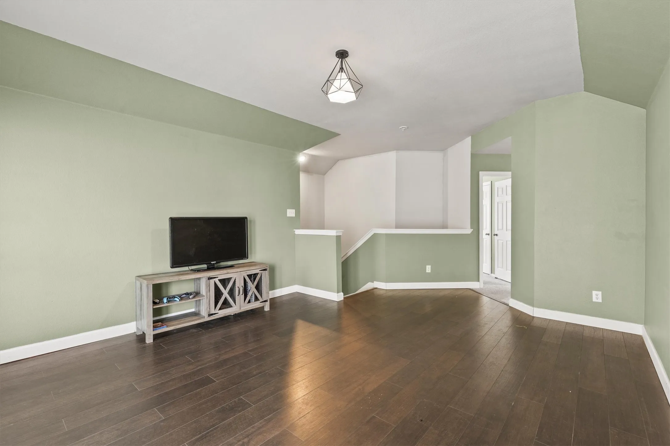 Spacious room featuring wood-finish flooring, a contemporary geometric ceiling light fixture, and a partial staircase