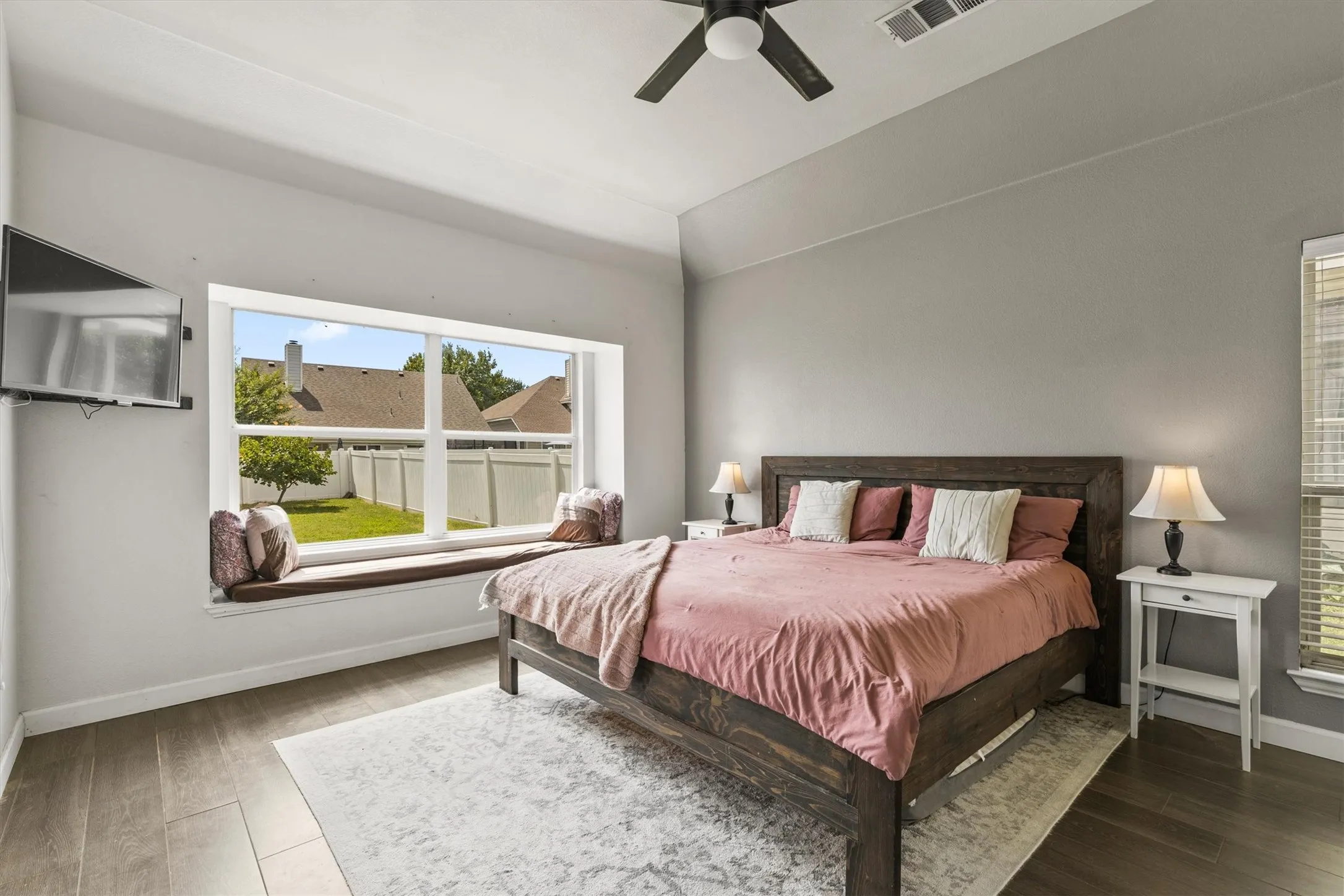 Spacious room featuring vaulted ceilings, wood-finish flooring, and a large window with an integrated seating bench