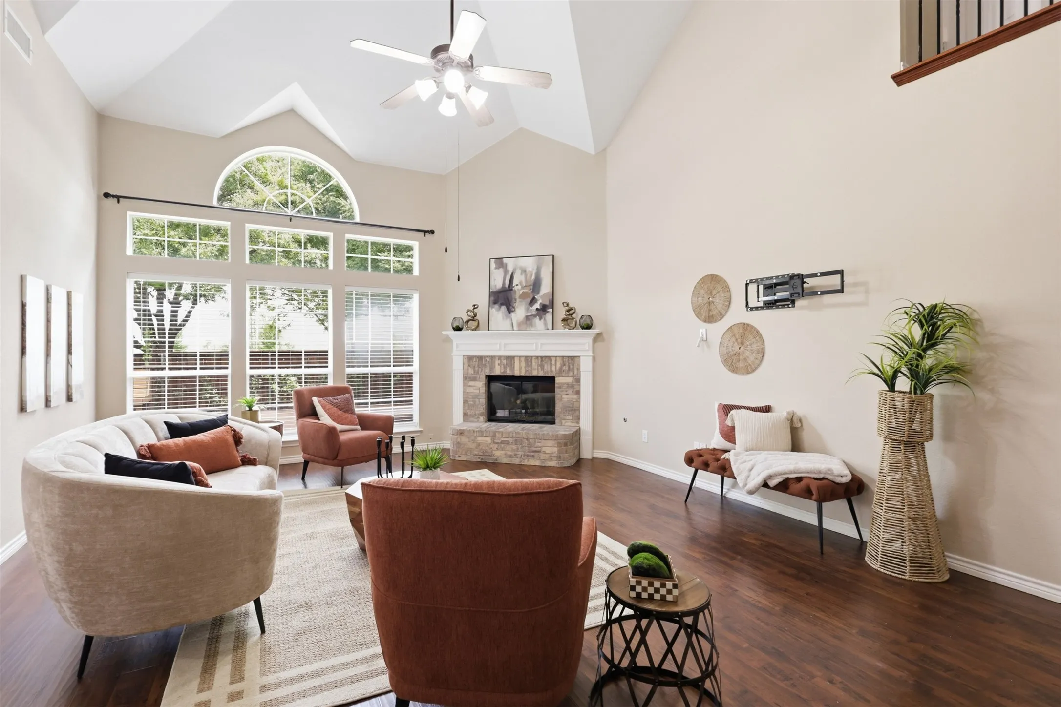Living space featuring high vaulted ceilings, expansive window wall with an arched transom, a stone fireplace with a mantle, laminate flooring, and a ceiling fan.