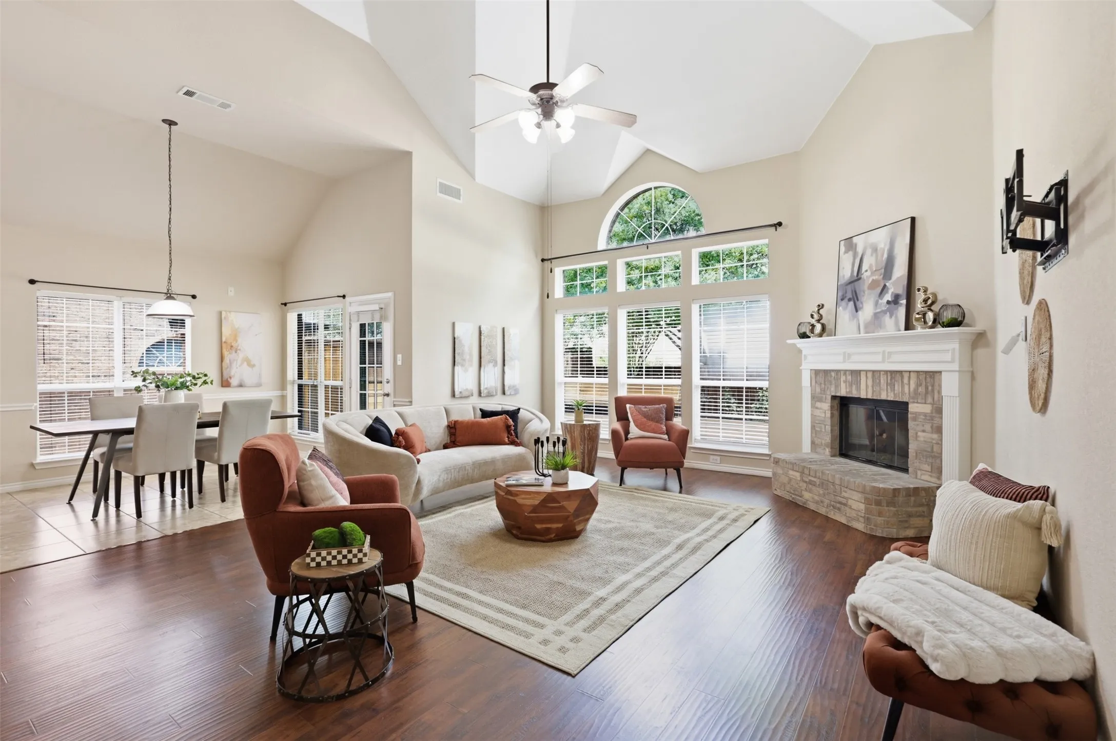 Vaulted ceilings enhance this living area featuring laminate flooring, a brick-clad fireplace with a classic mantel, and ample natural light through large windows, including an arched transom.