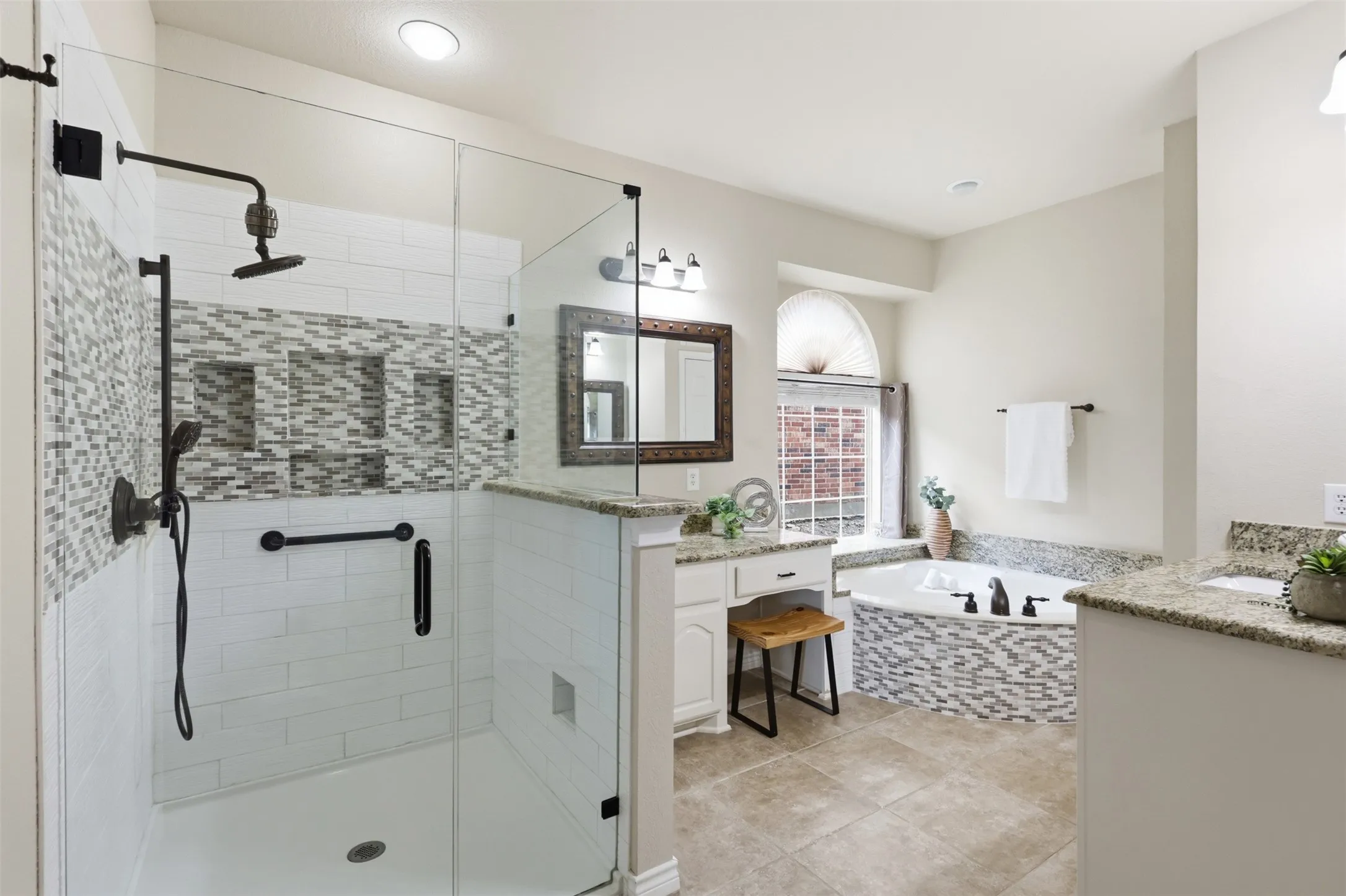Spacious Ensuite bathroom featuring a glass-enclosed shower with subway tile and mosaic accents, a built-in garden tub with mosaic tile surround, dual vanities with granite countertops, and tile flooring.