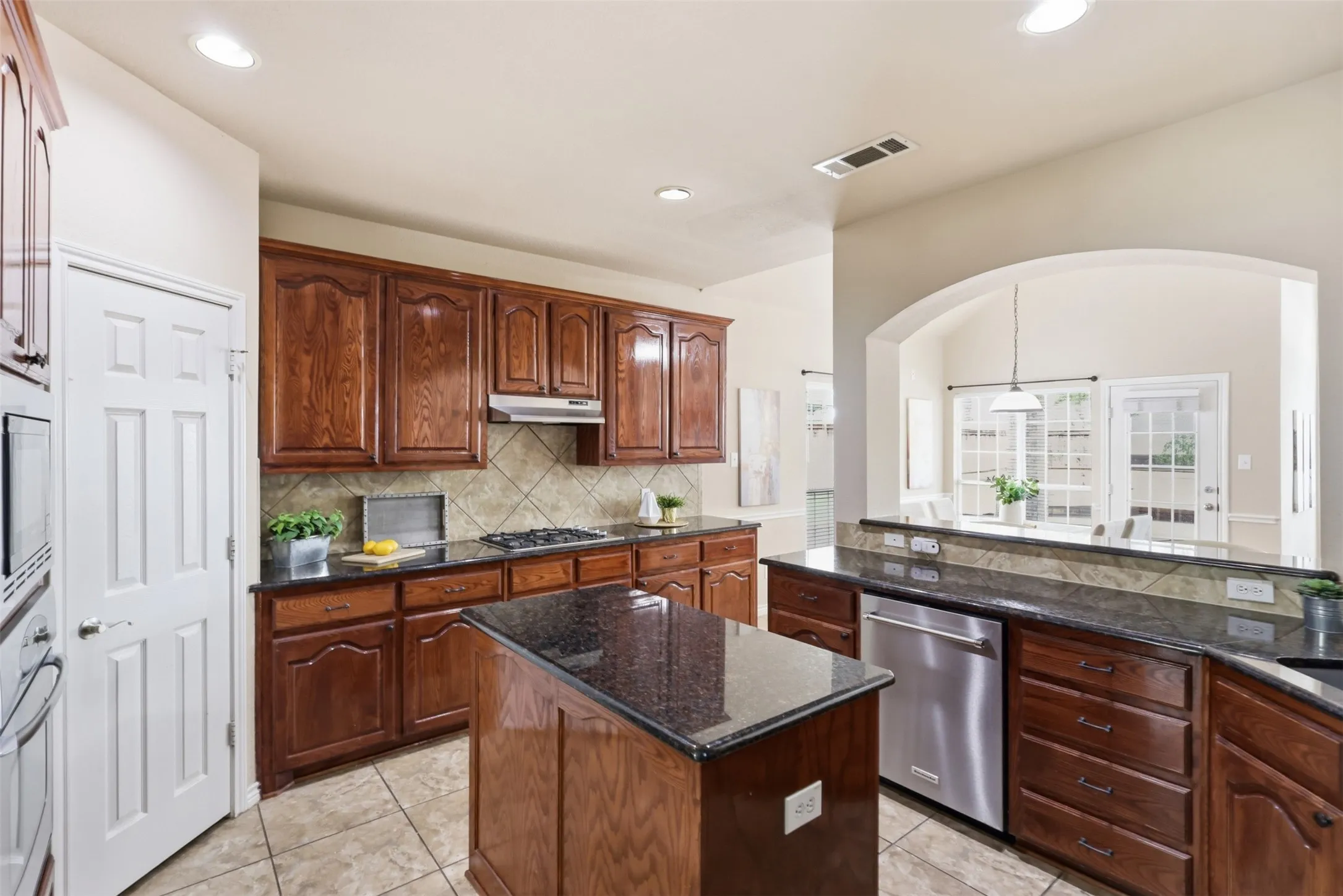 Kitchen featuring dark wood cabinetry, granite countertops, a tiled backsplash, and stainless steel appliances, including a built-in microwave, oven and dishwasher.
