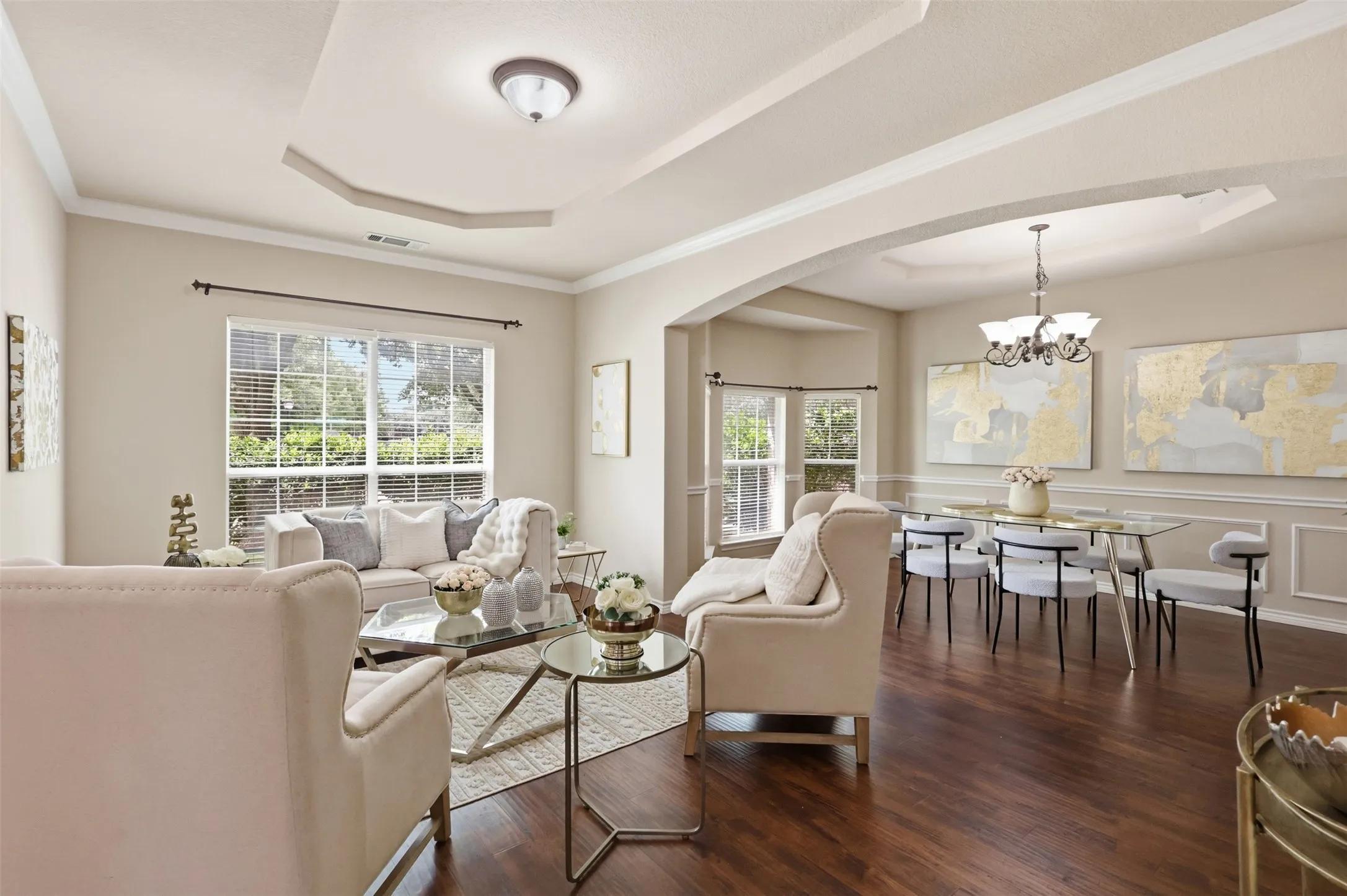 Spacious formal living area featuring tray ceilings, arched doorways, expansive window, and laminate flooring.