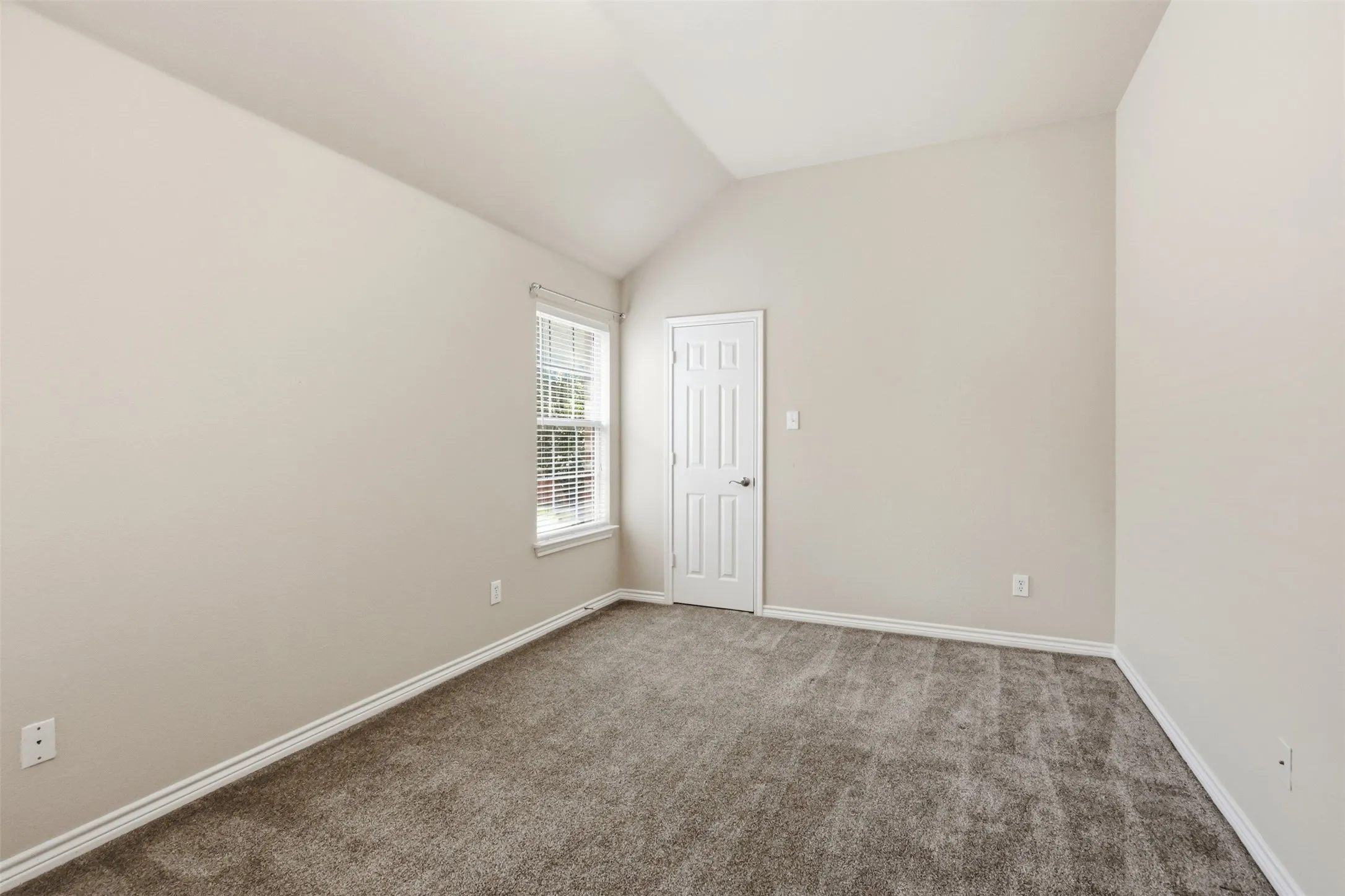 Bedroom with vaulted ceiling, neutral wall tones, and plush carpeting.