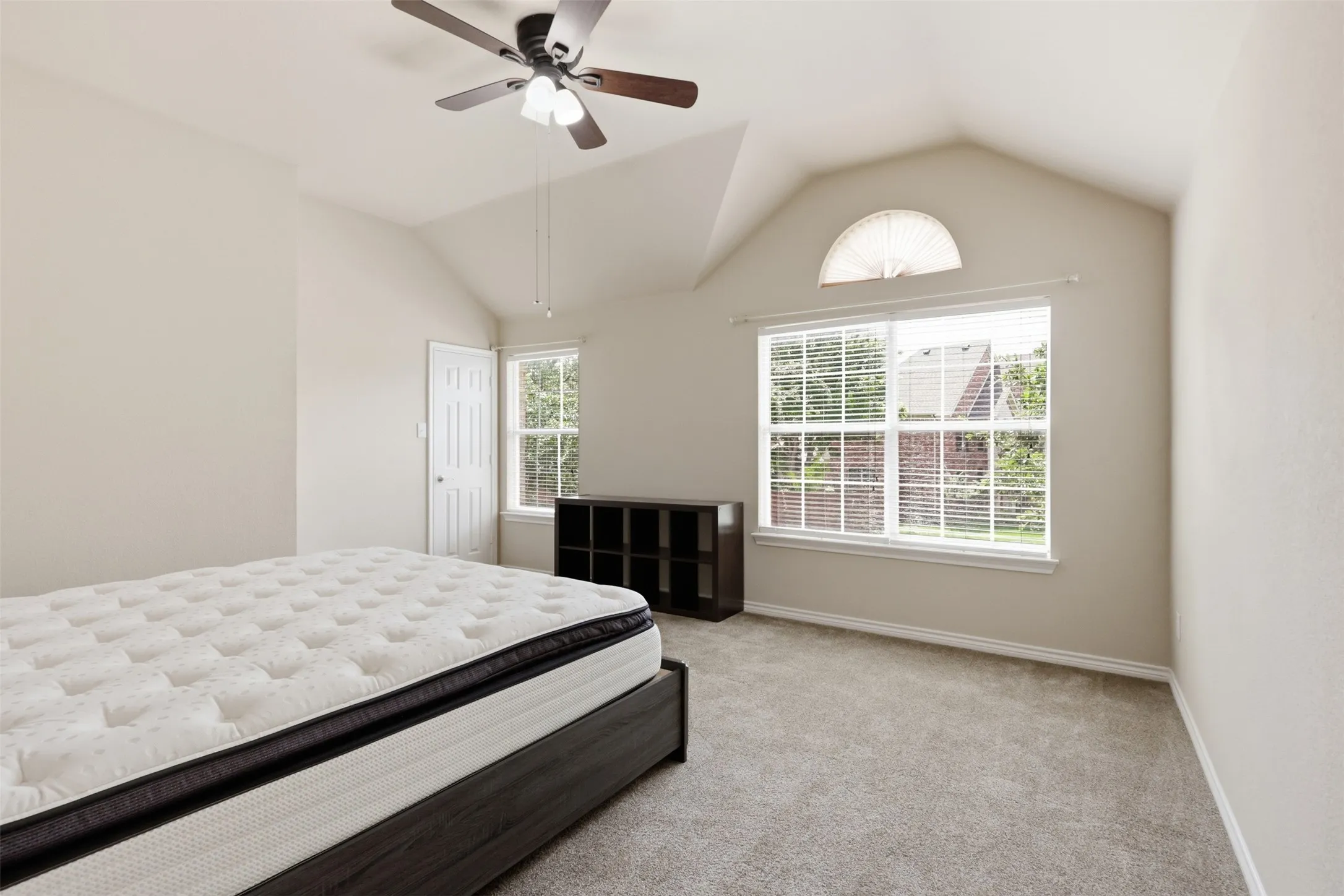 Vaulted ceiling Bedroom featuring a ceiling fan, large window with blinds, and an arched transom window.