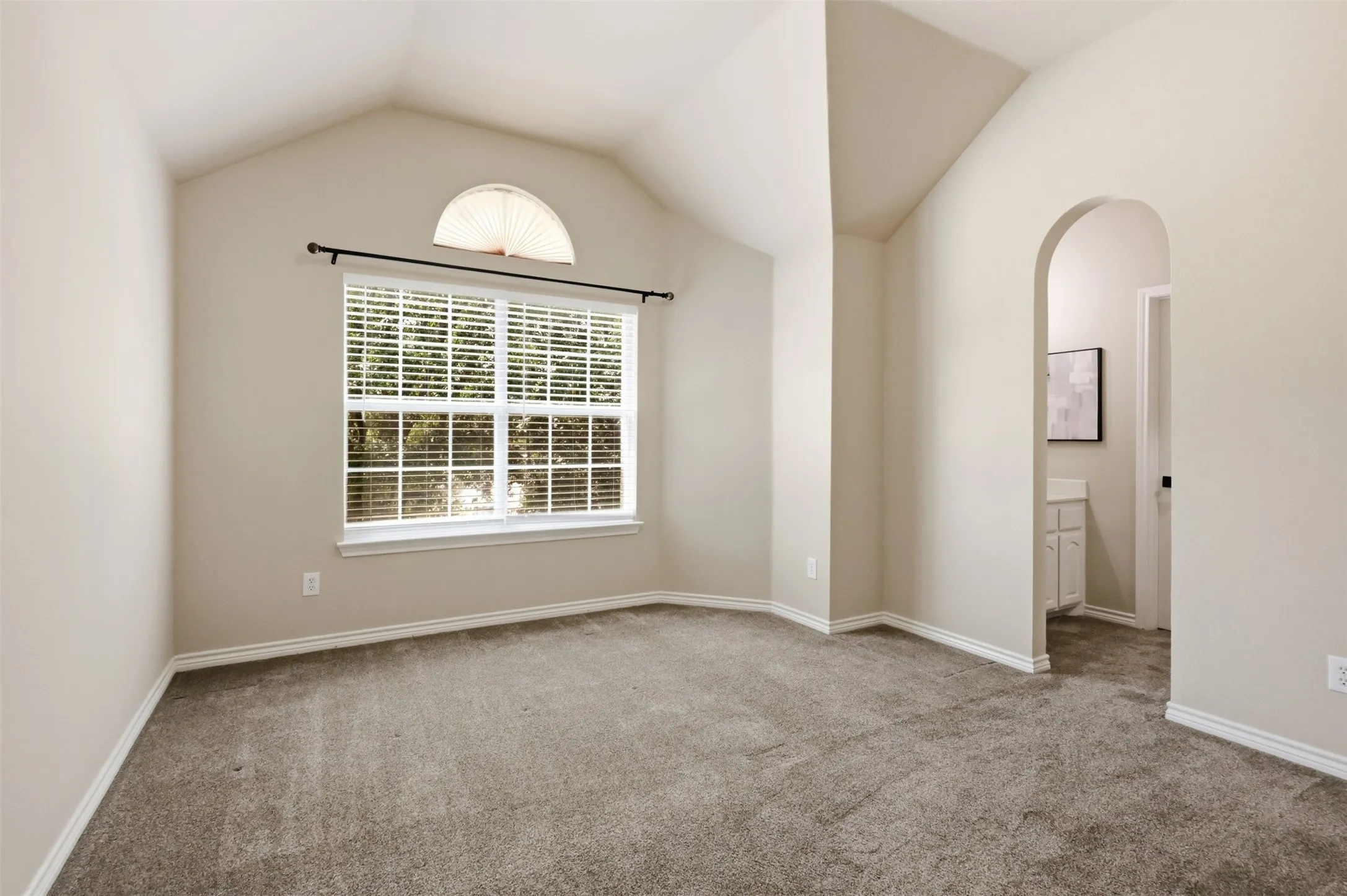 Vaulted ceiling bedroom with a large window featuring white blinds and an arched transom window above with a Jack and Jill Bathroom.
