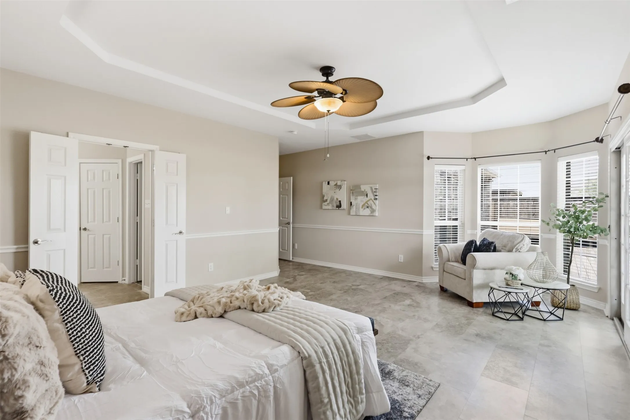 Spacious Primary Bedroom featuring tray ceilings, neutral tone walls with wainscoting, and large windows with blinds.
