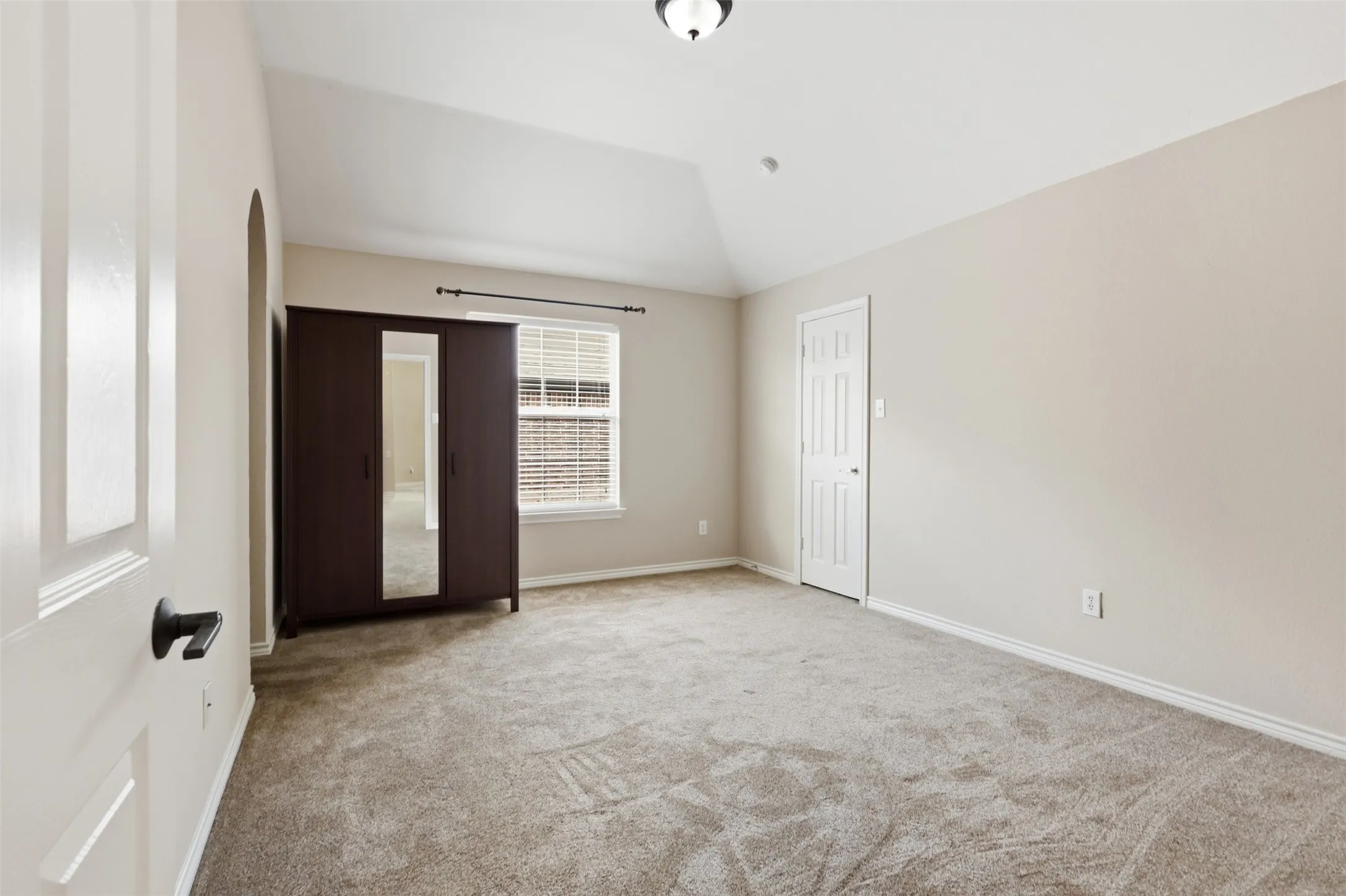 Bedroom featuring vaulted ceilings, neutral wall tones, plush carpeting, and a window with blinds.