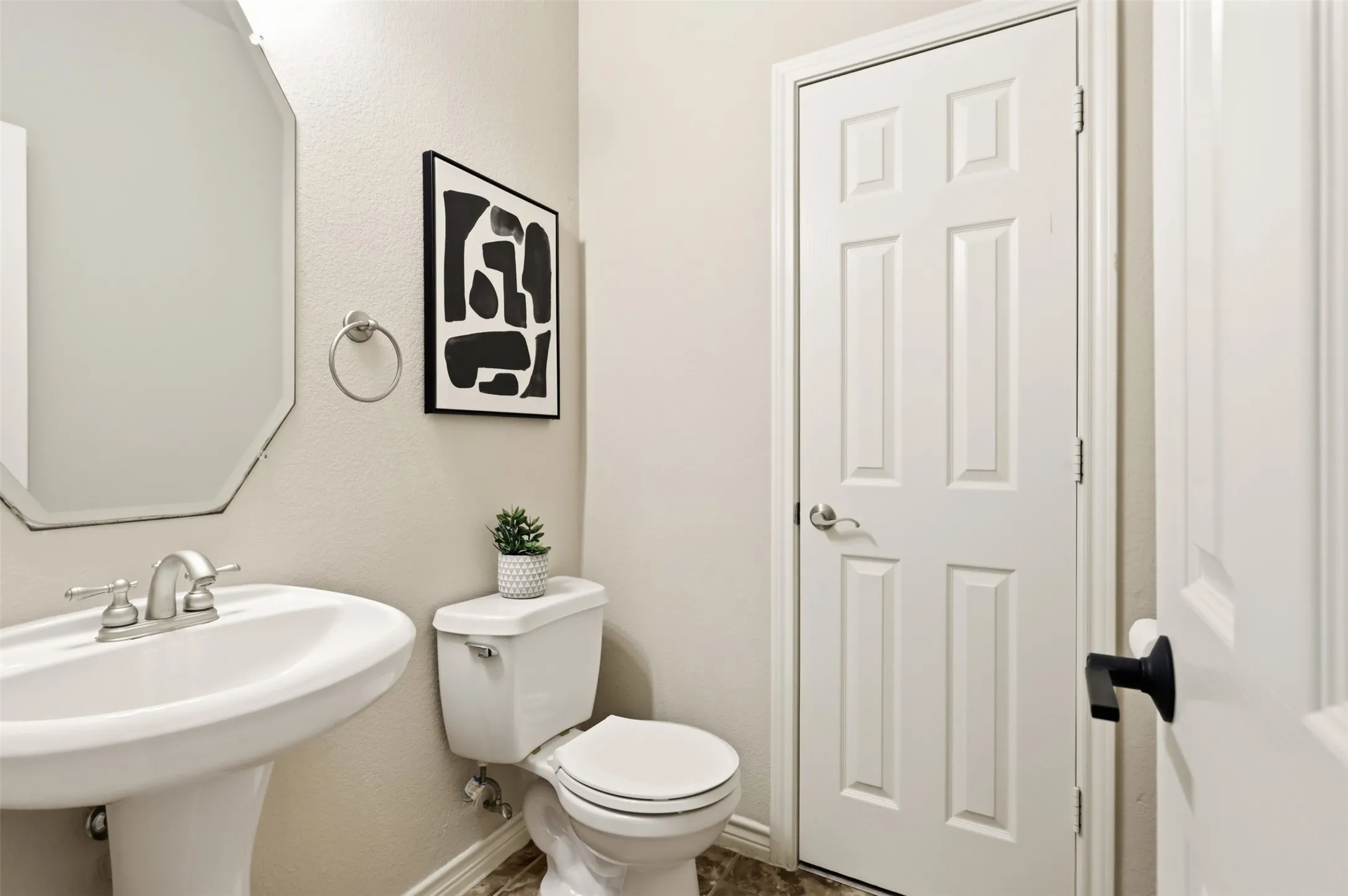 Pedestal sink with brushed nickel faucet, octagonal wall-mounted mirror, white commode, and panel interior doors with varied hardware.