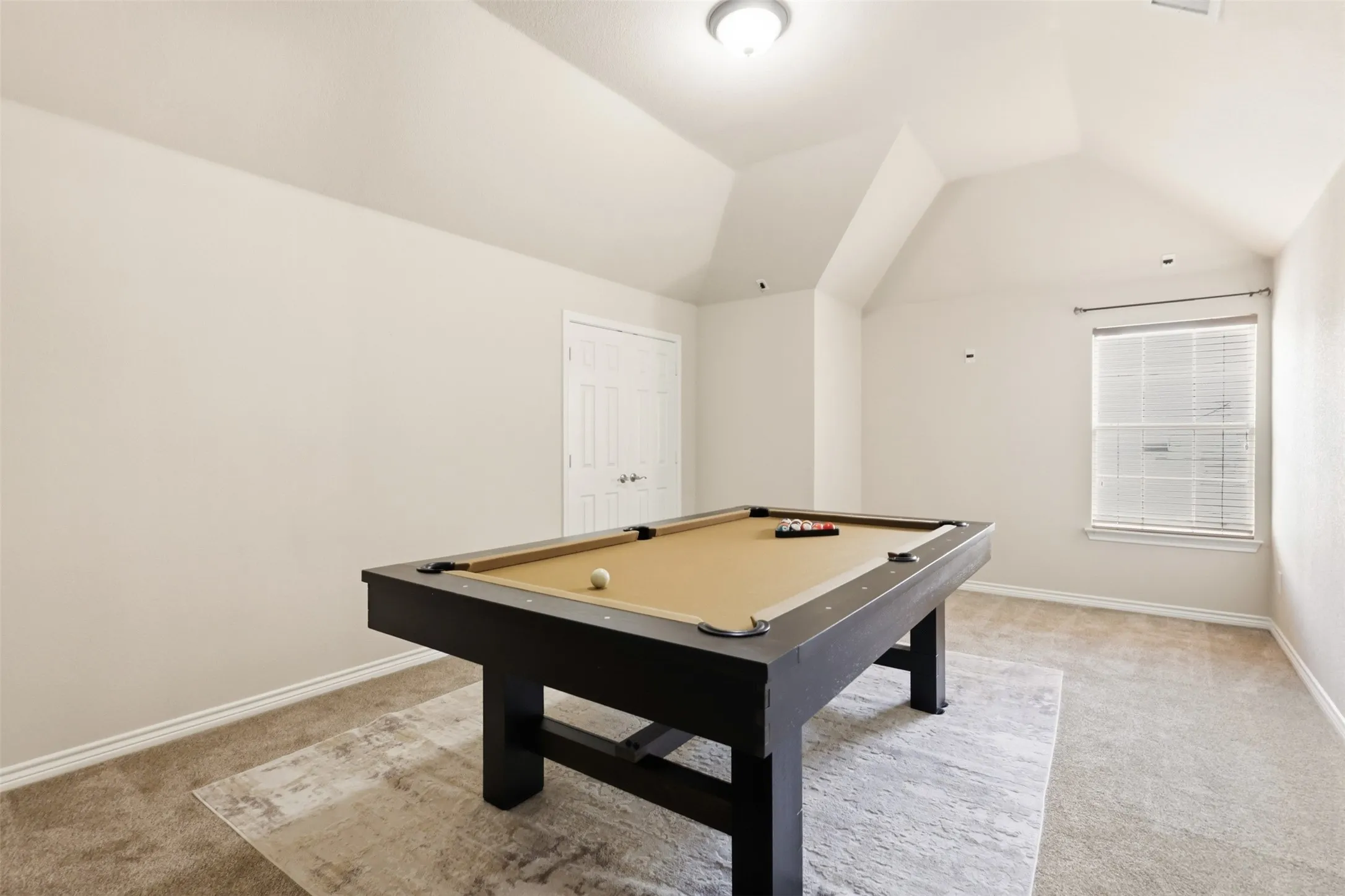 Spacious bonus room perfect as a media room or game room featuring vaulted ceilings, neutral carpet, and a window with blinds.