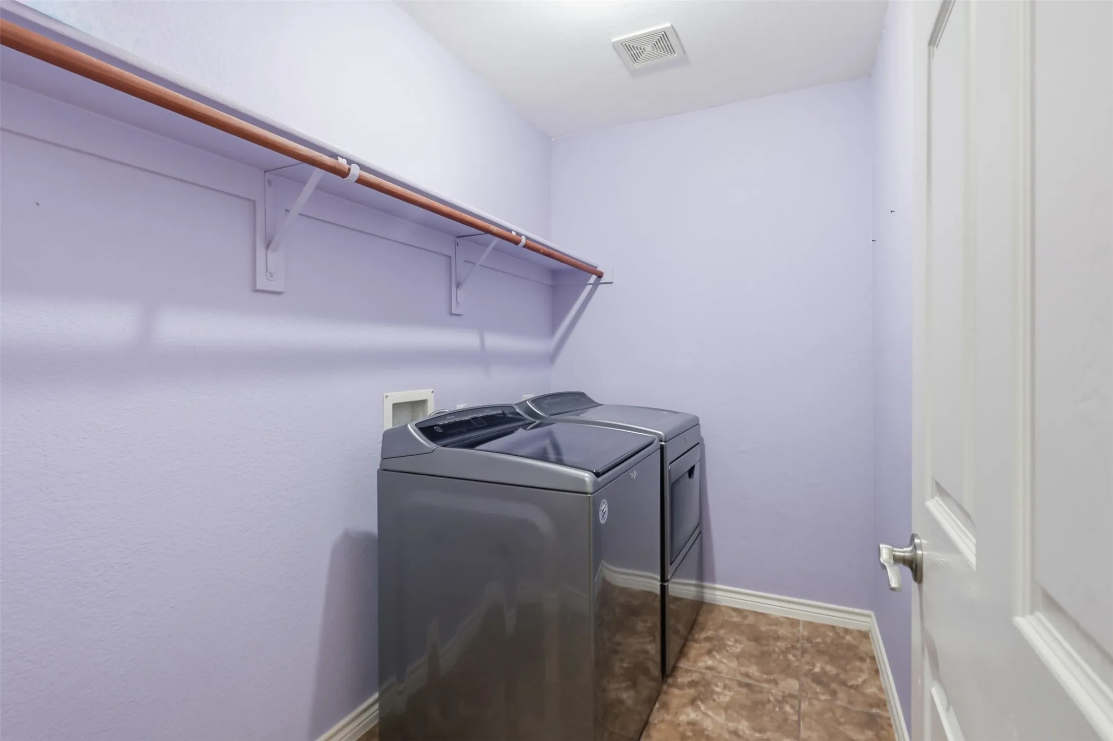 Dedicated laundry area featuring a hanging rod and tile flooring.