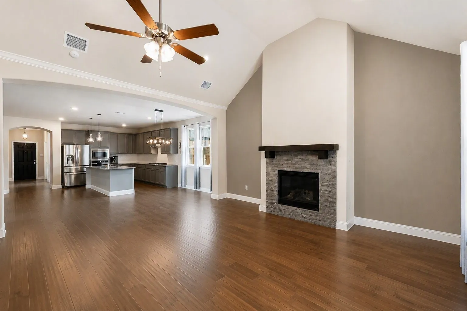Open-concept living space featuring wood-finish flooring, a vaulted ceiling, and a fireplace with a stone surround and wood mantle
