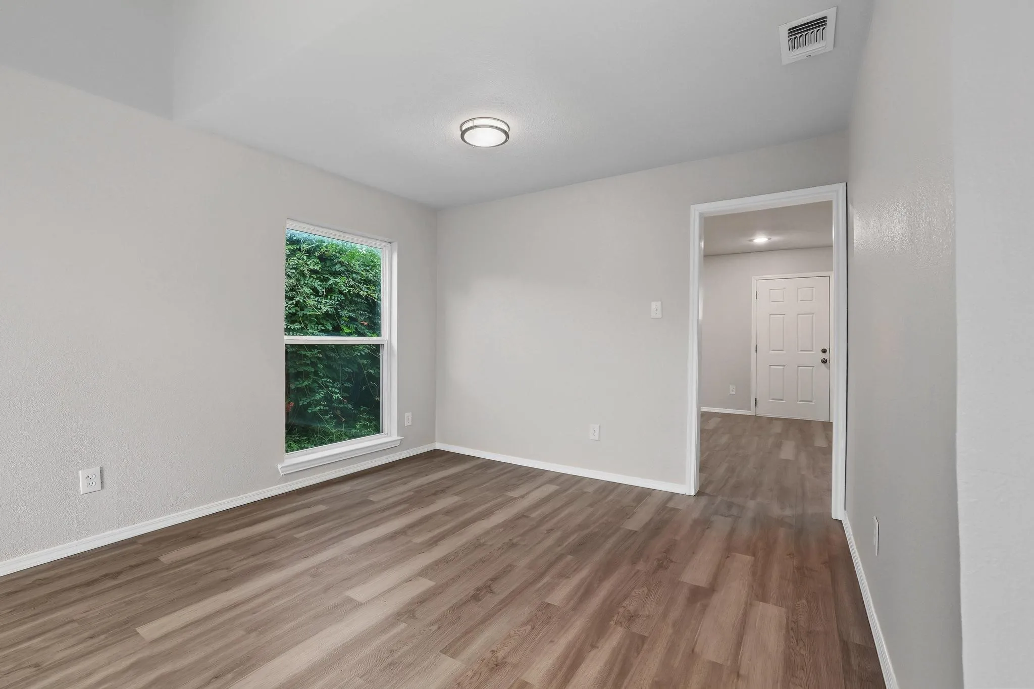 Spacious room featuring wood-finish flooring, light gray walls, white trim, and a contemporary flush-mount ceiling light
