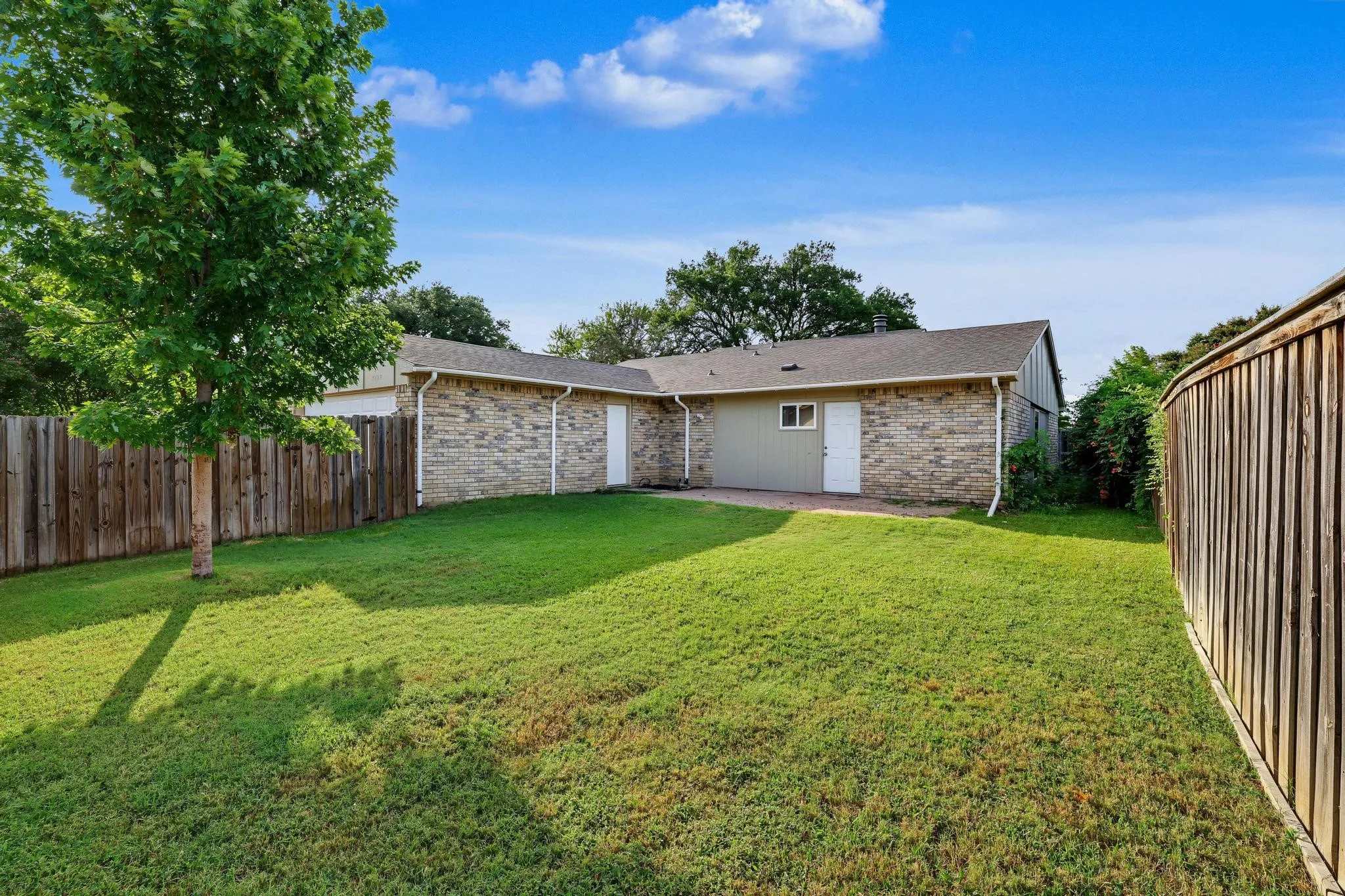 Expansive backyard featuring a lush lawn, mature shade tree, and wood privacy fencing