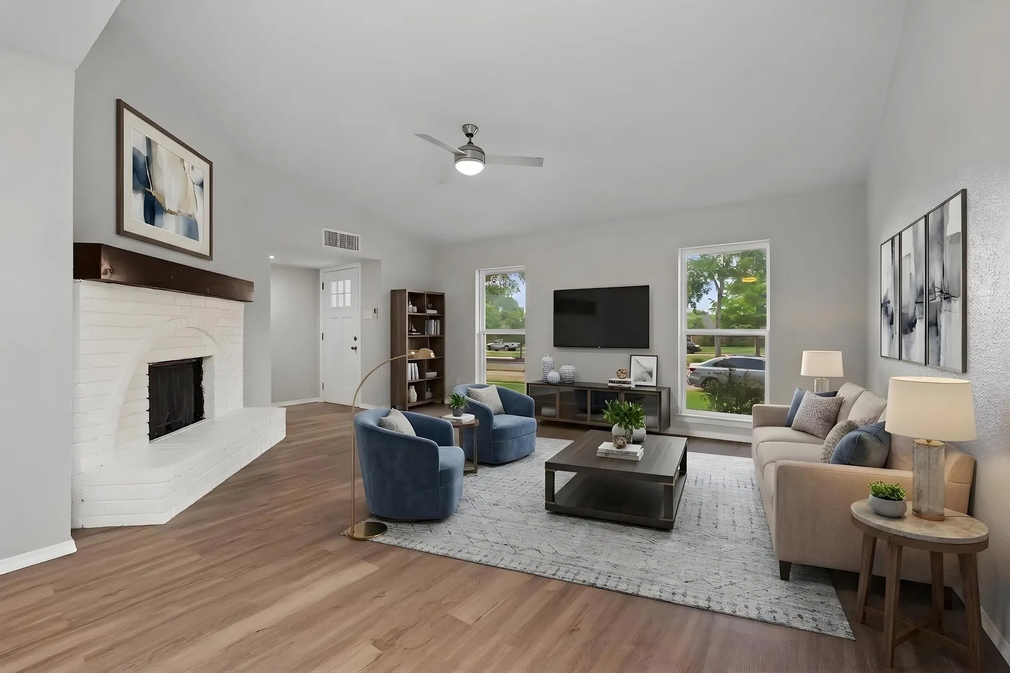 Spacious living area featuring a vaulted ceiling, wood-finish flooring, and a white-painted brick fireplace