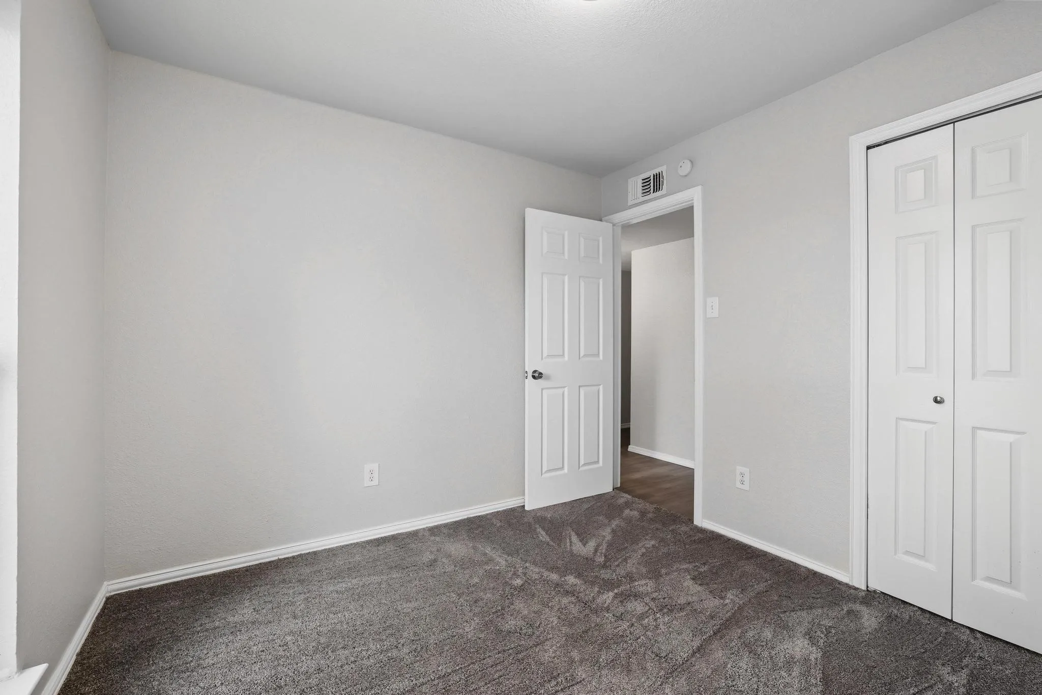 Interior room featuring light gray wall paint, gray carpeting, a six-panel interior door, white baseboards, and a white bi-fold closet door