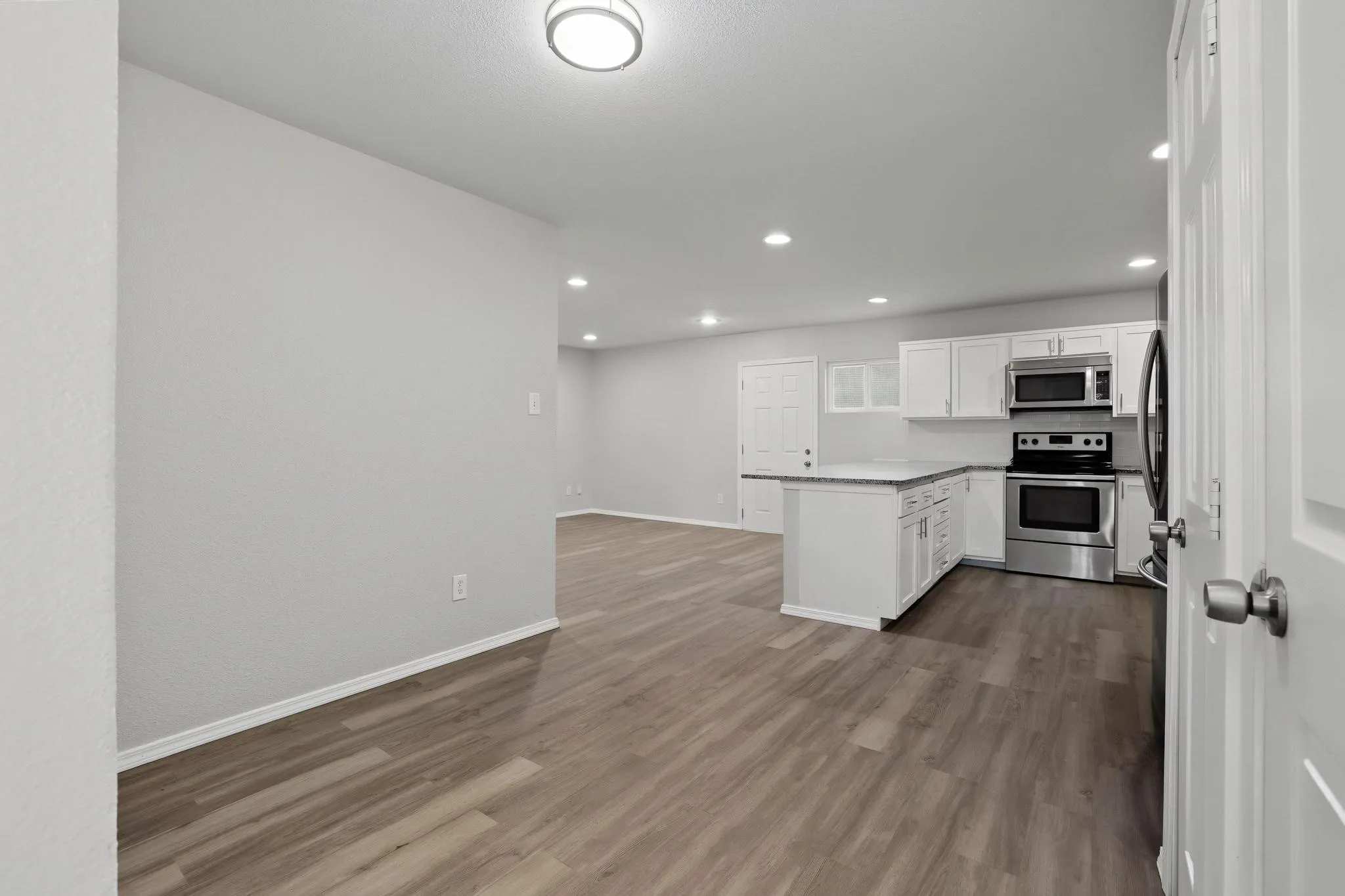 Open-concept kitchen and living area featuring wood-finish flooring, recessed lighting, white cabinetry, a kitchen island, and stainless steel appliances