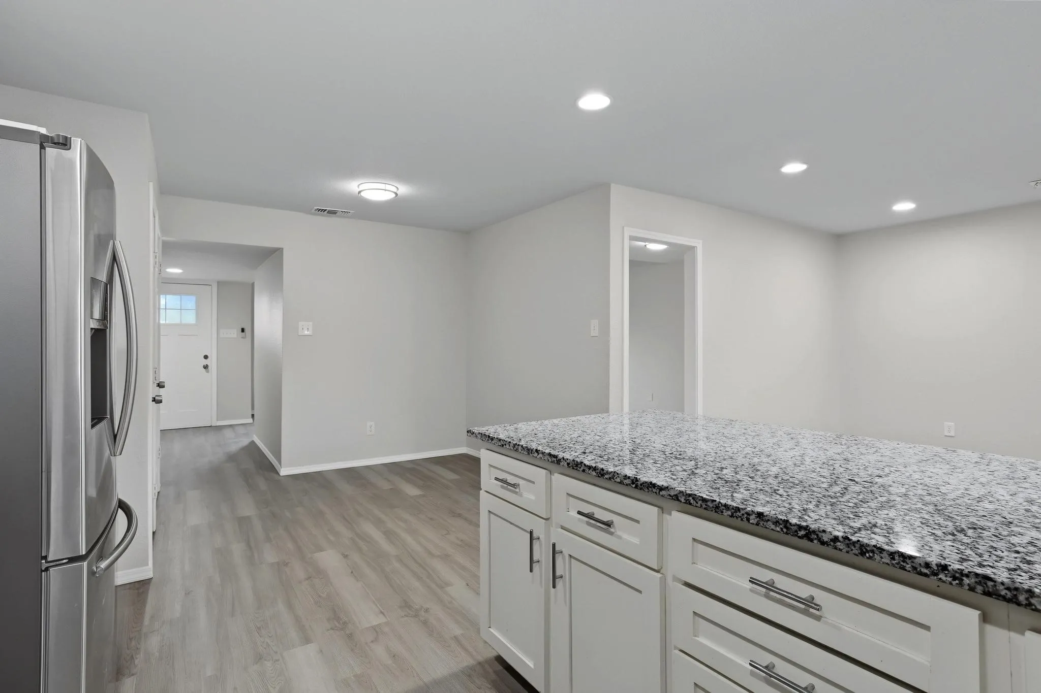Spacious interior featuring a kitchen island with a granite-style countertop, white cabinetry with contemporary hardware, recessed lighting, and wood-finish flooring