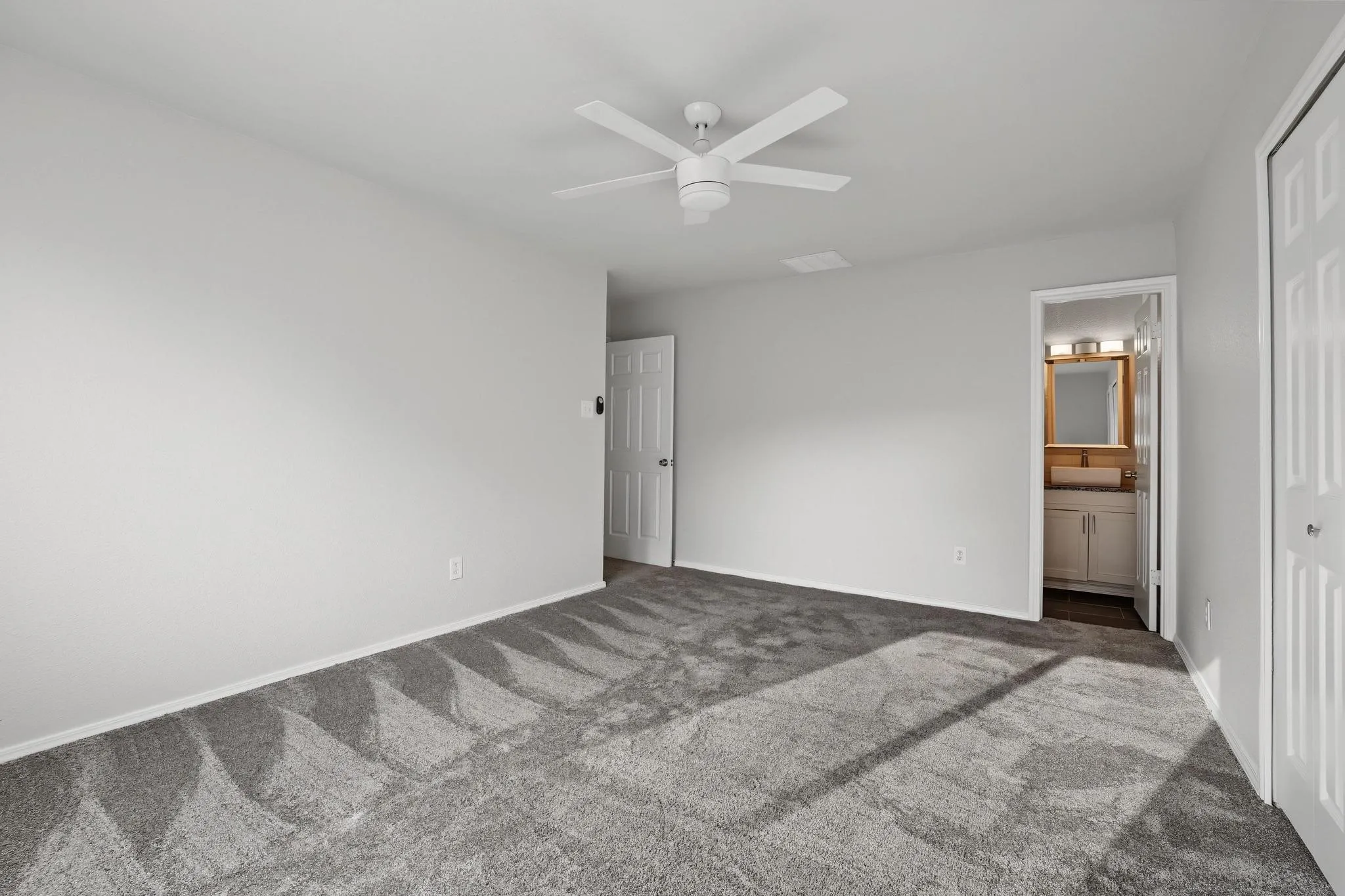 Spacious room with light gray walls, gray patterned carpet, and a white ceiling fan