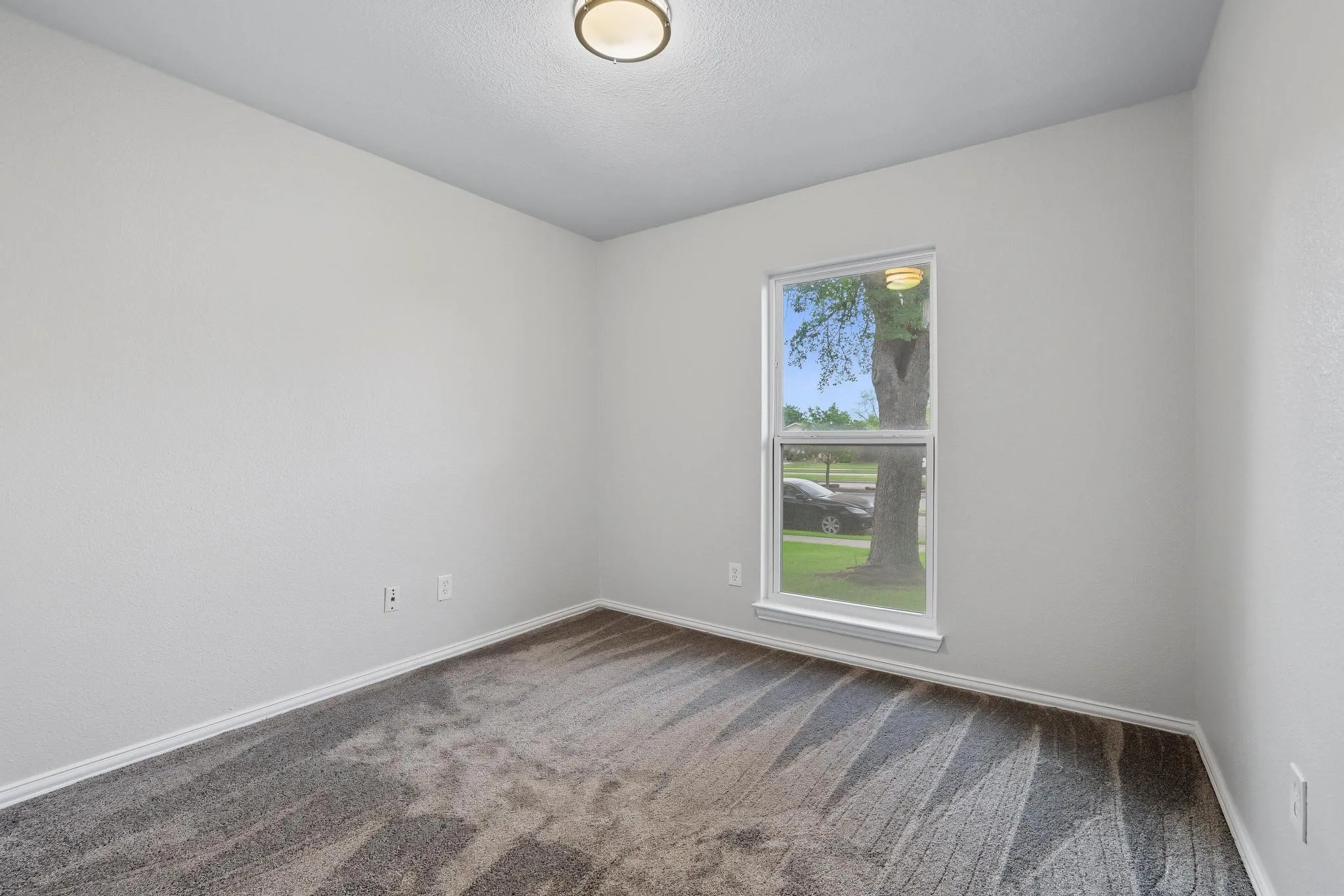 Neutral-toned interior featuring a single window, a flush-mount ceiling light, and patterned carpeting