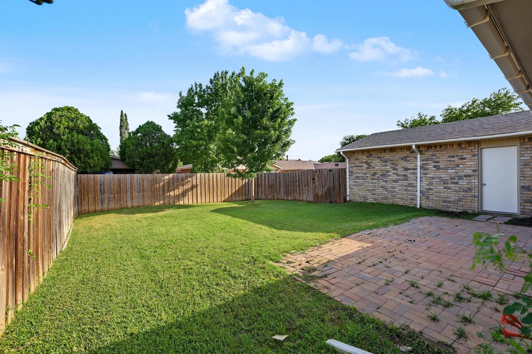Expansive backyard featuring a manicured lawn, full privacy fencing, and a red brick paver patio