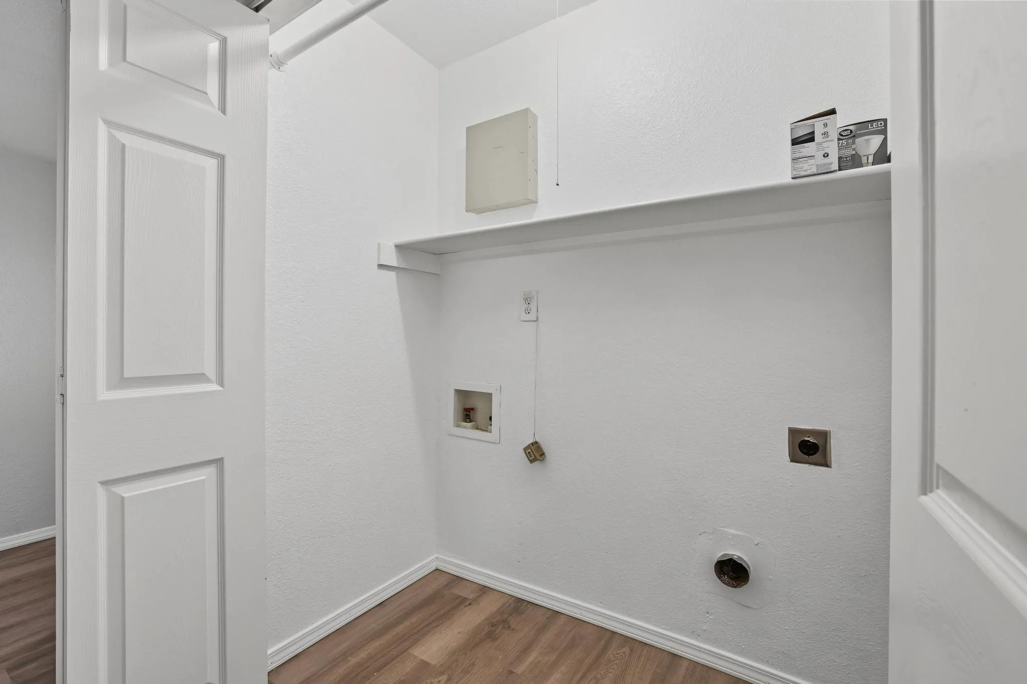 Dedicated utility area featuring wood-finish flooring, white walls, and a built-in storage shelf
