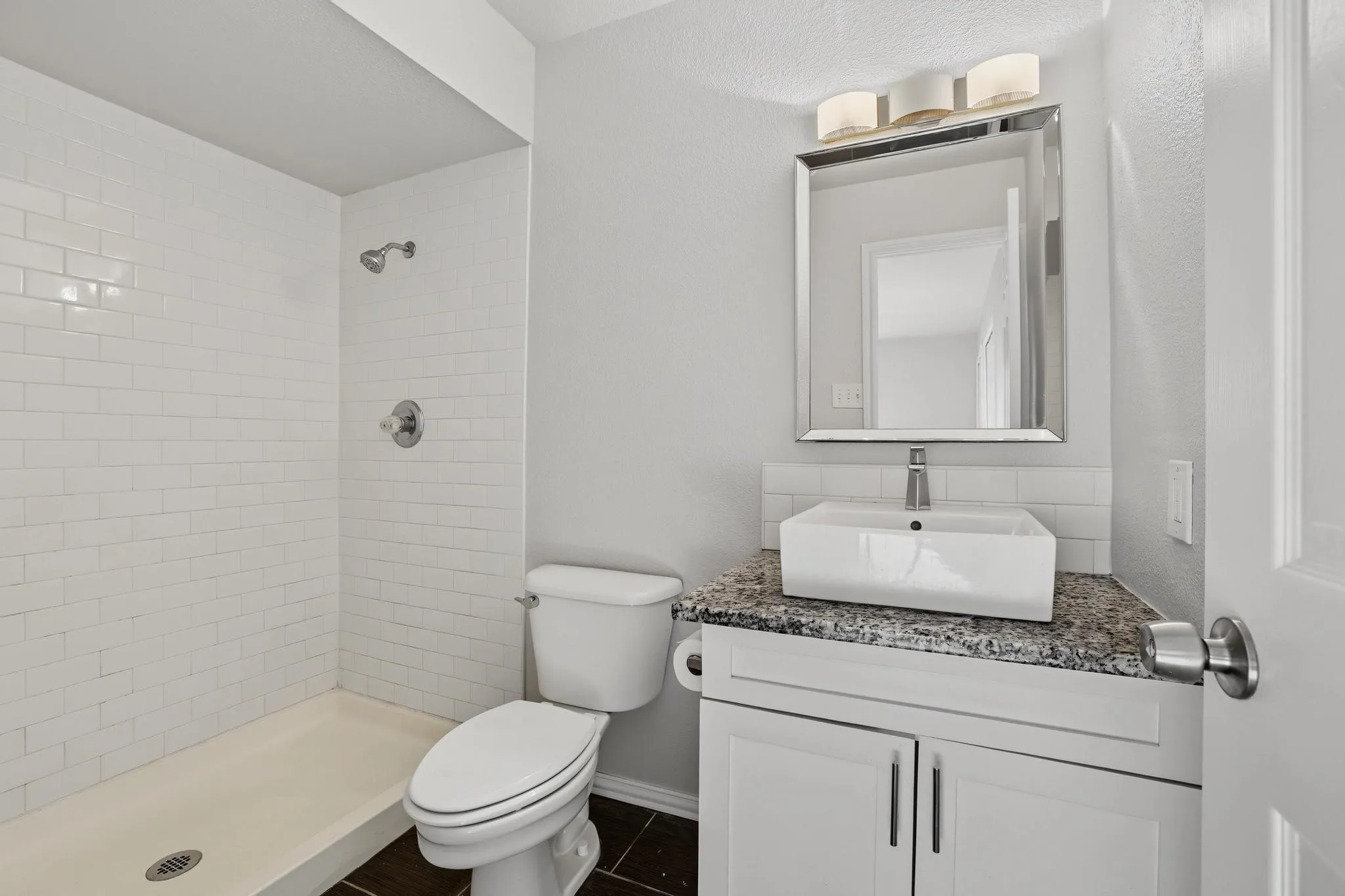 Bathroom featuring a white subway tile shower, a rectangular vessel sink, a speckled countertop, and white cabinetry